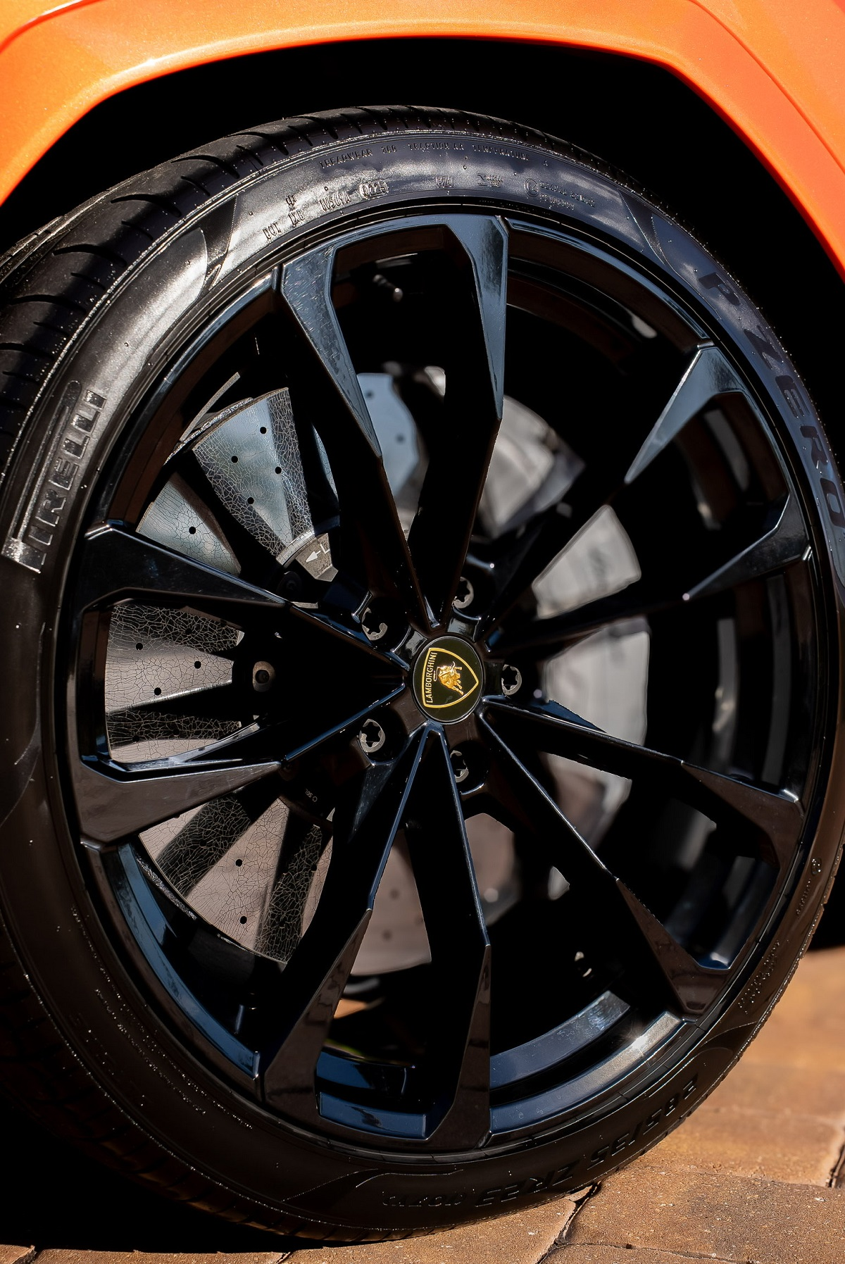 Black alloy car wheel with wet tire under orange body panel, close-up.
