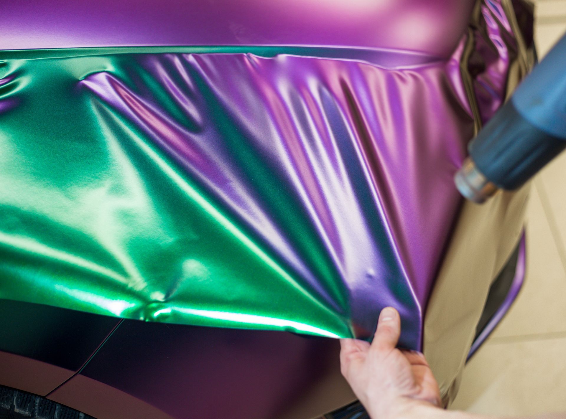 Hands smoothing shiny purple and green wrapping film with a heat gun