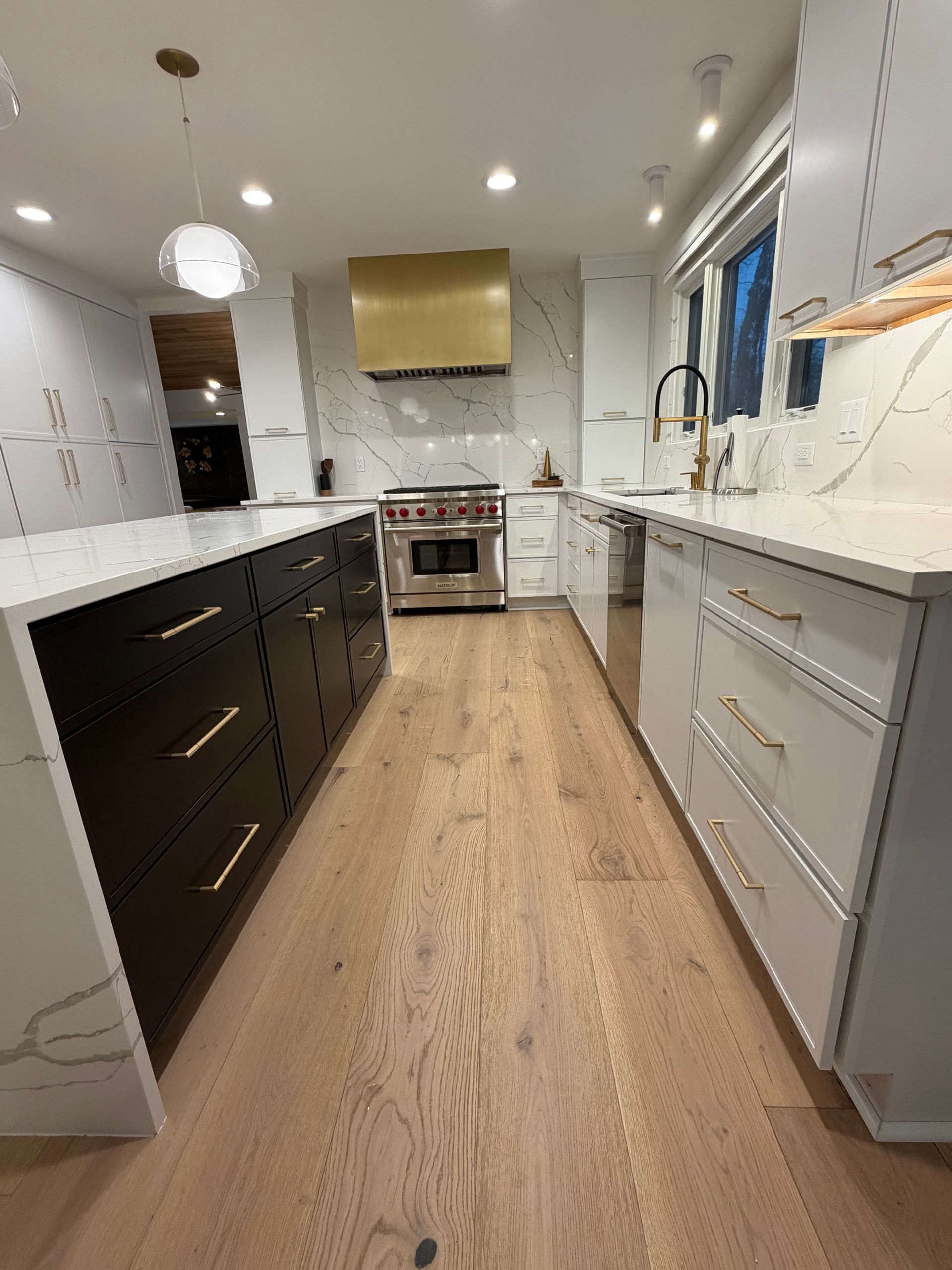 Bright modern kitchen with white and dark cabinets, wood floor, and stainless steel appliances.