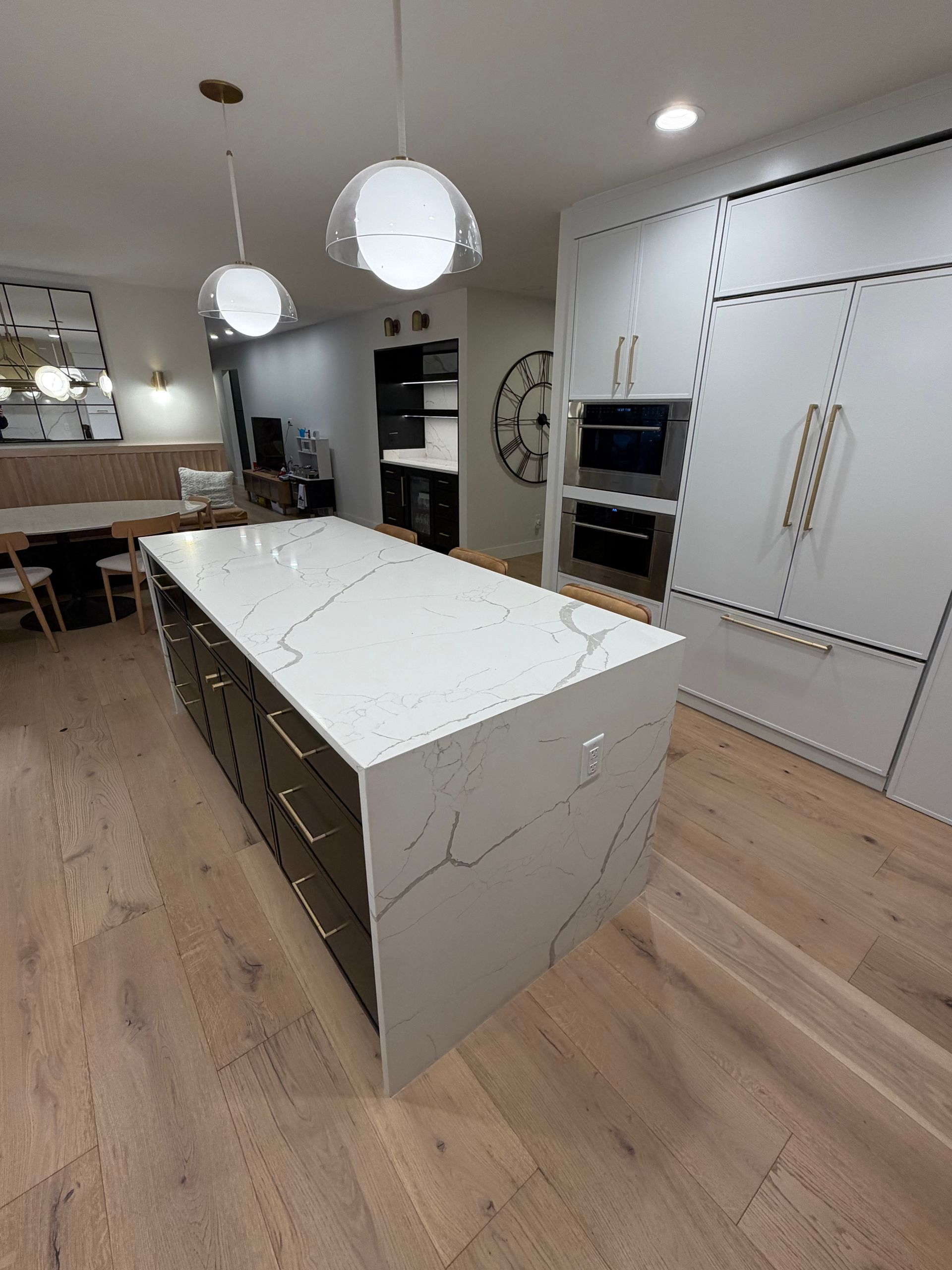 Modern kitchen with a large white marble island, wood floors, pendant lights, and built-in appliances.