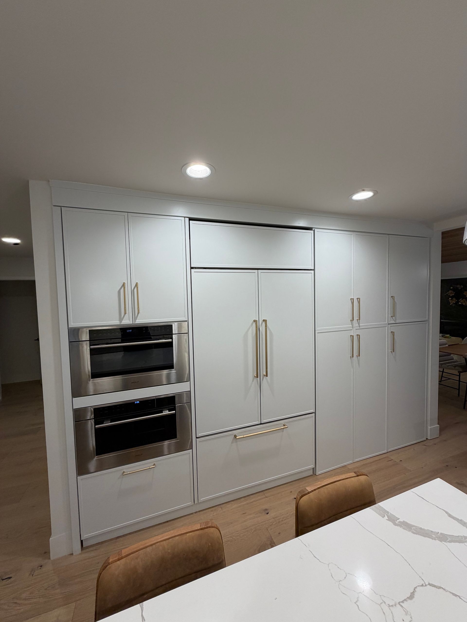 Modern white kitchen wall with built-in ovens, cabinets, and a marble countertop in the foreground