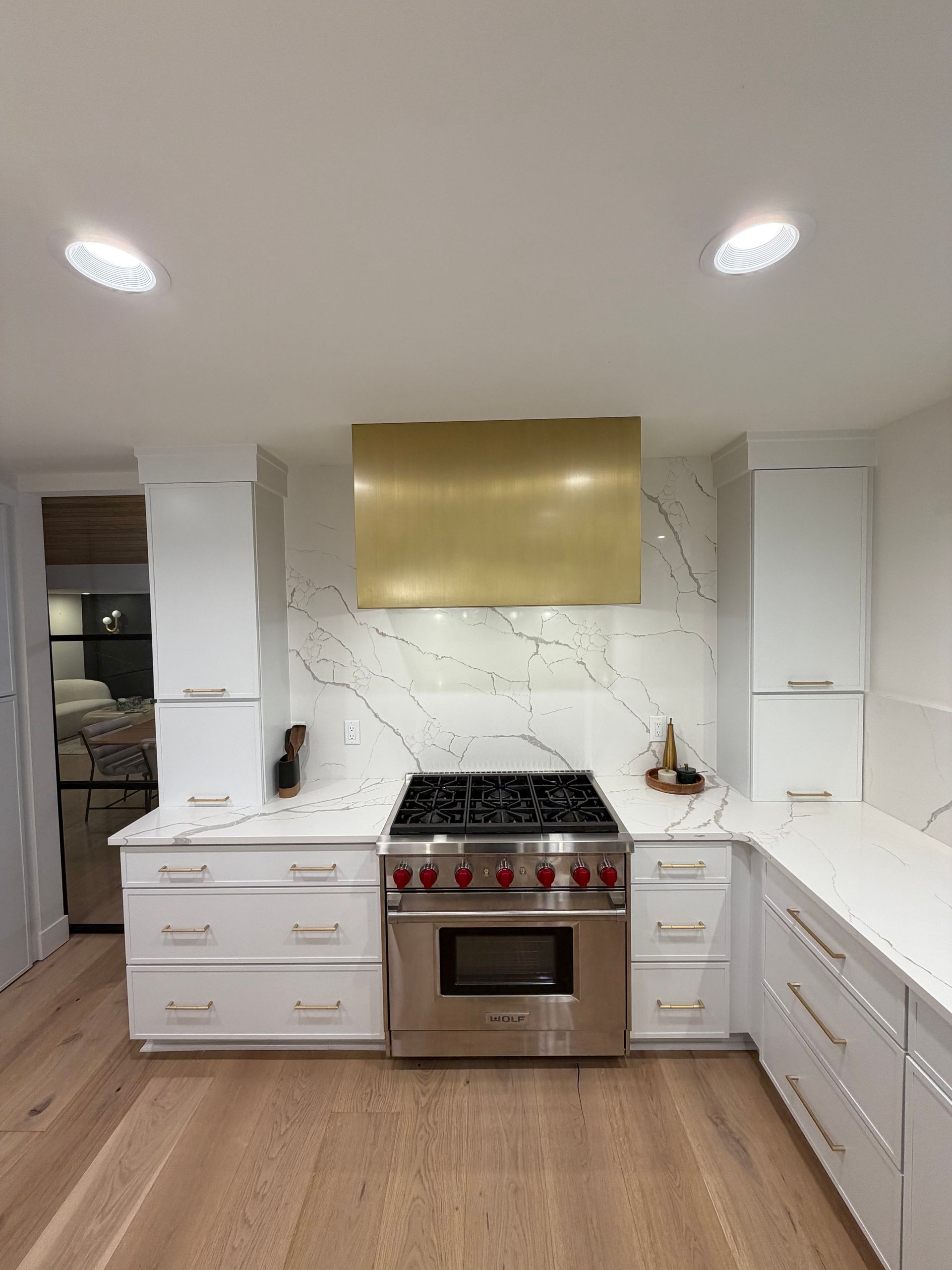 Modern white kitchen with gold range hood, stainless stove, and wood floors
