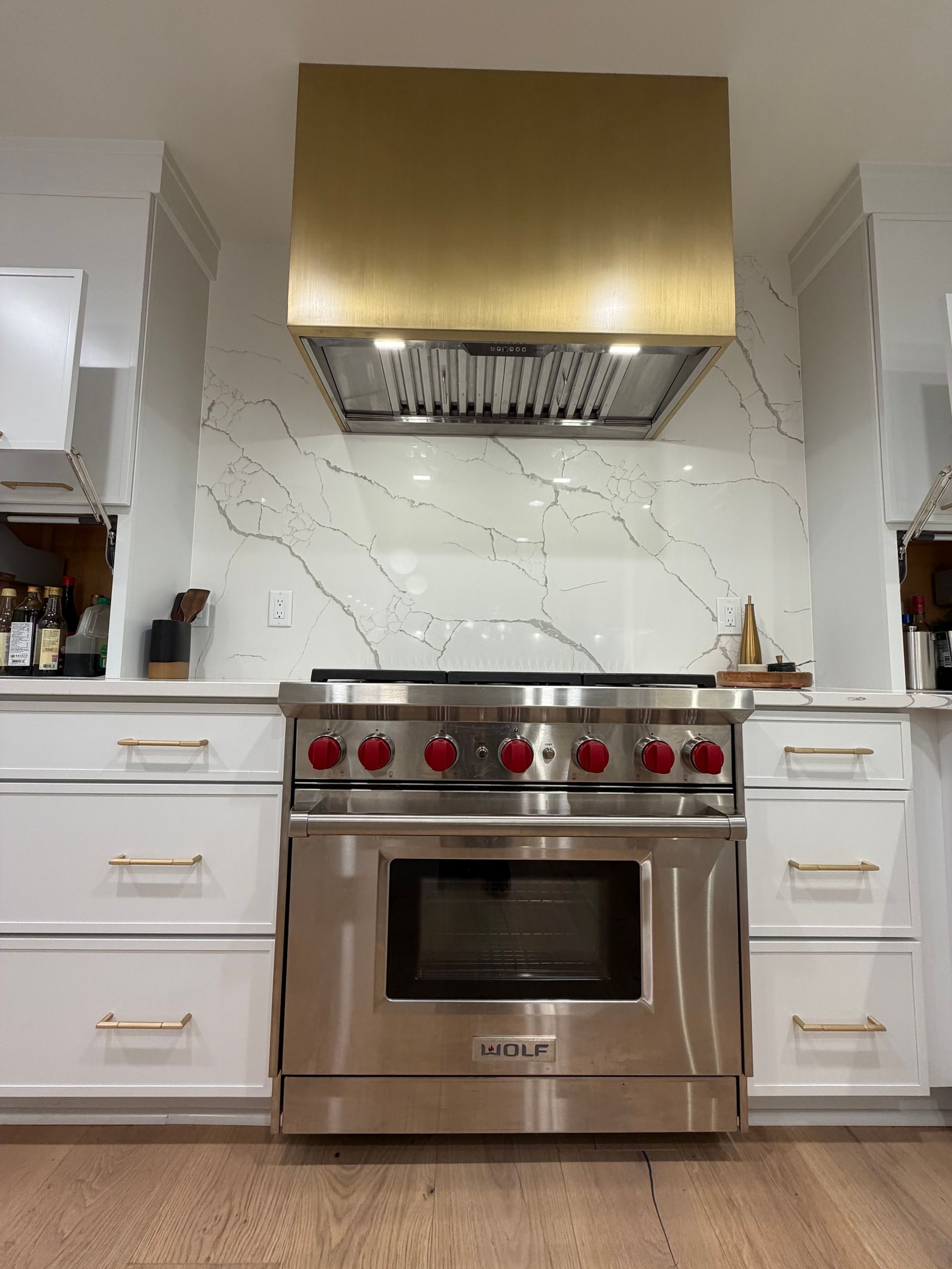 Modern kitchen with stainless steel range, red knobs, white cabinets, and gold range hood