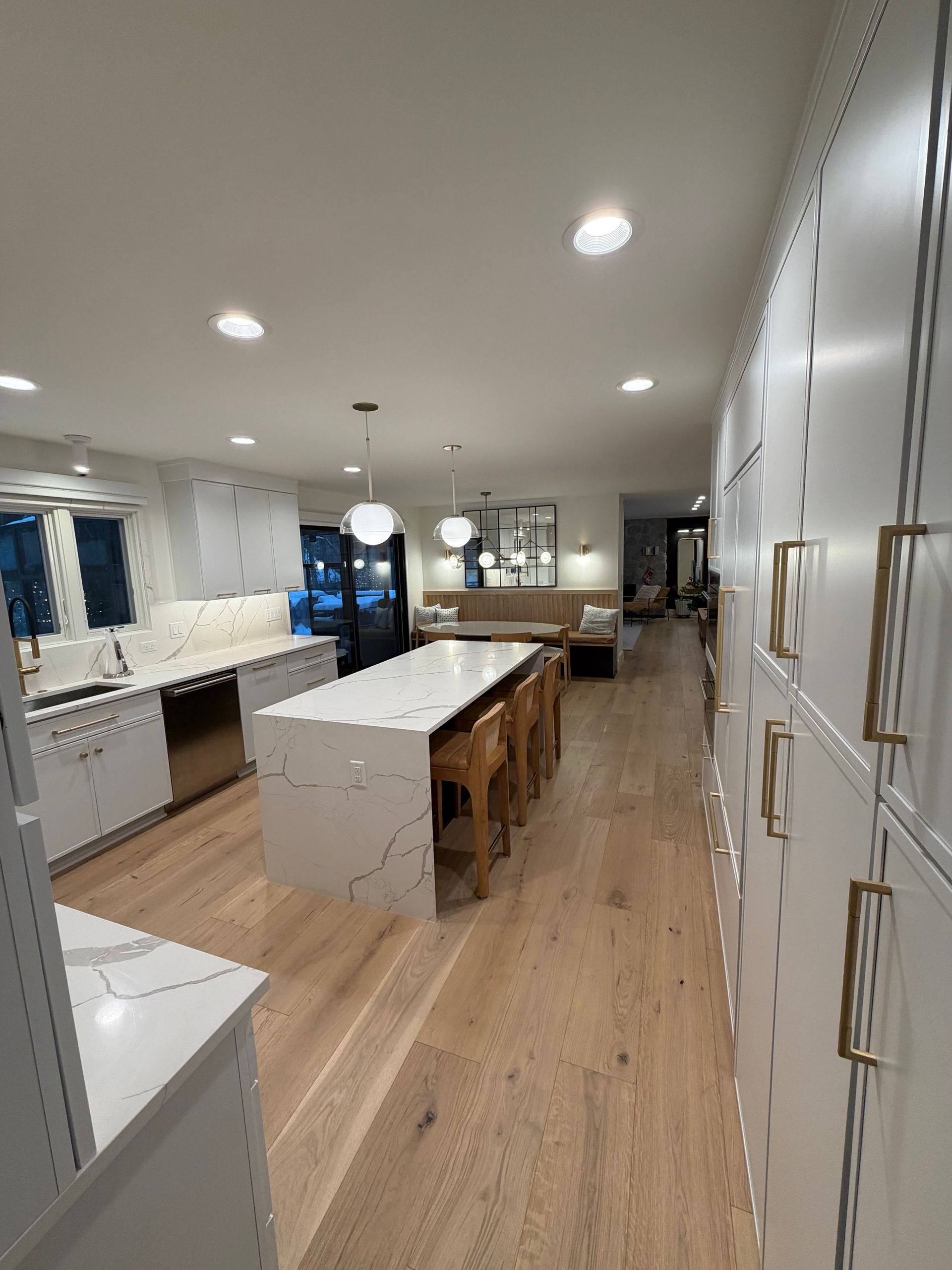 Modern white kitchen with large island, wood floors, recessed lights, and built-in cabinets