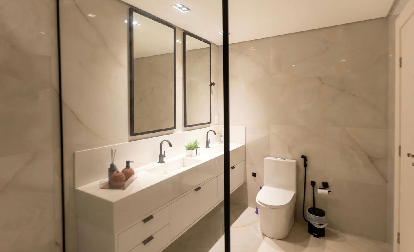 Modern bathroom with large vanity, double mirrors, glass shower, and toilet with toilet brush holder.