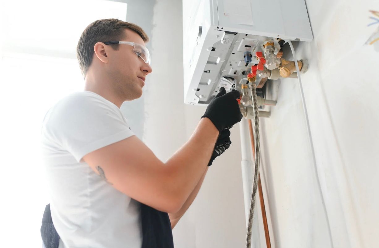 Technician repairing a wall-mounted boiler with tools in a bright room