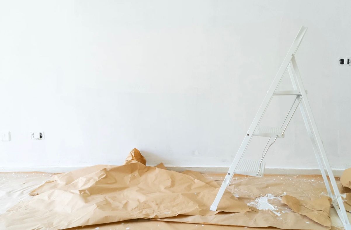 Empty room with white walls, covered floor, and a white step ladder on the right