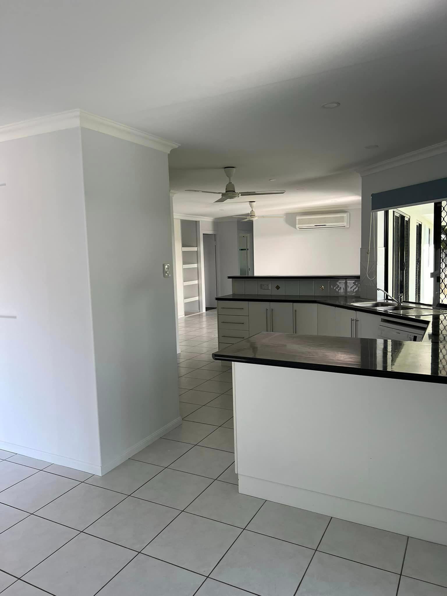 An Empty Kitchen with White Cabinets and Black Counter Tops — Darren Smith Painting Pty Ltd in Mackay, QLD