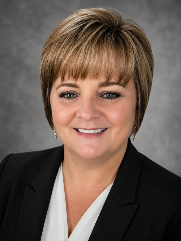 Professional headshot of a smiling person in a black blazer on a gray background