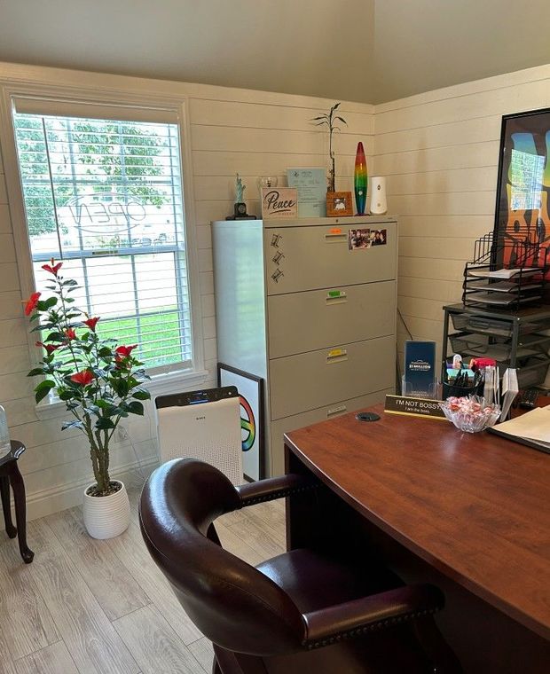 Home office with white walls, a desk, chair, refrigerator, and potted plant by a window.