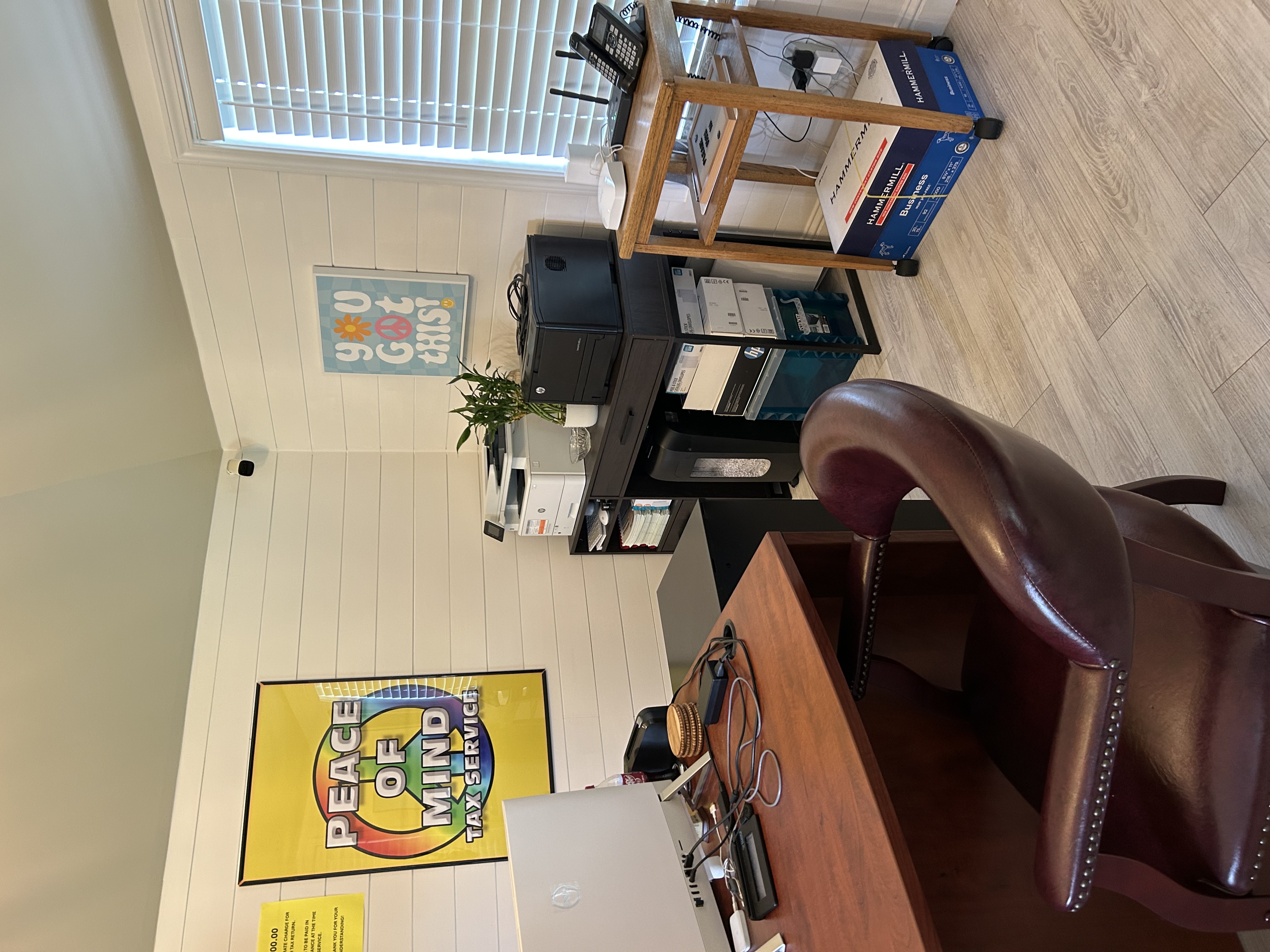Home office with wooden desk, leather chair, computer monitor, printer, shelves, and colorful wall art.