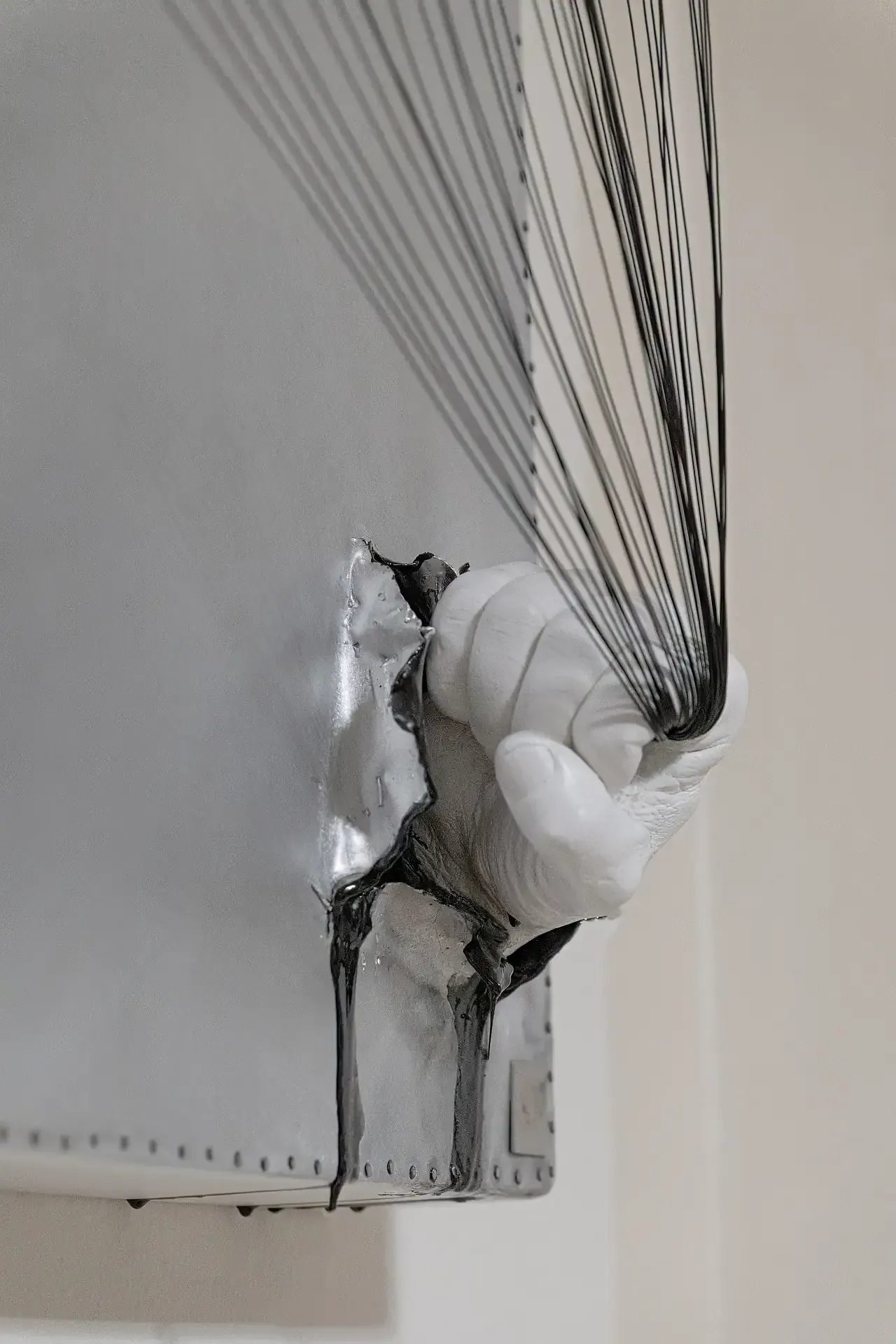 Dettaglio di scultura su tela in resina e leghe metalliche, mano (d'artista) che impugna fili in acciao.