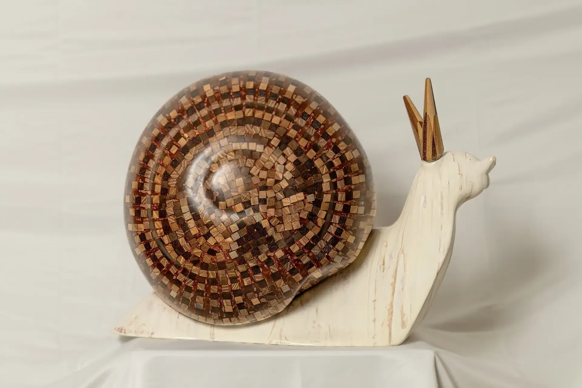 Scultura di una chiocciola con corpo in gesso ceramico bianco crema e guscio sferico a mosaico composto da tasselli di legno inglobati in resina trasparente. Opera materica dell'artista Guerino Rusconi.
