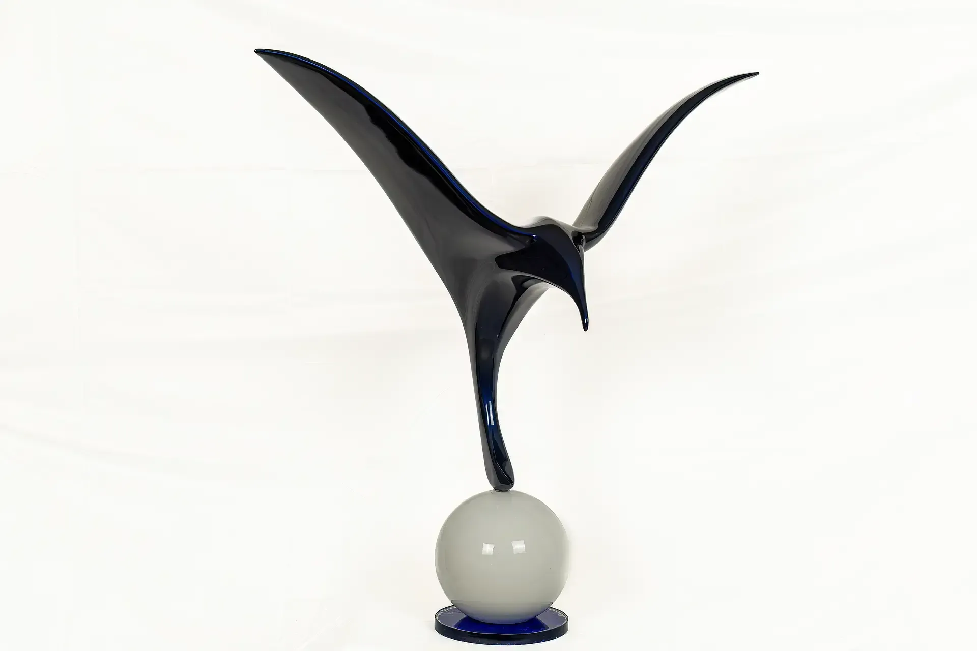 Scultura di gabbiano stilizzato con struttura interna in legno rivestita in resina epossidica blu lucido, poggiante su una sfera bianca e base circolare blu scuro di Guerino Rusconi.