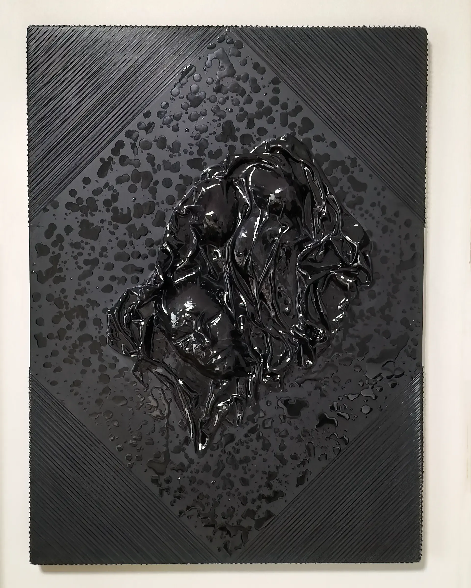 Scultura in resina tridimensionale, telo di raso imbevuto di resina e fili di alluminio su pannello ligneo. L'opera, realizzata dall'artista Guerino Rusconi, presenta una superficie materica nei toni del nero con fili in lega metallica. Al centro troviamo un volto umano astratto in resina nera. Texture lucida e riflettente. 