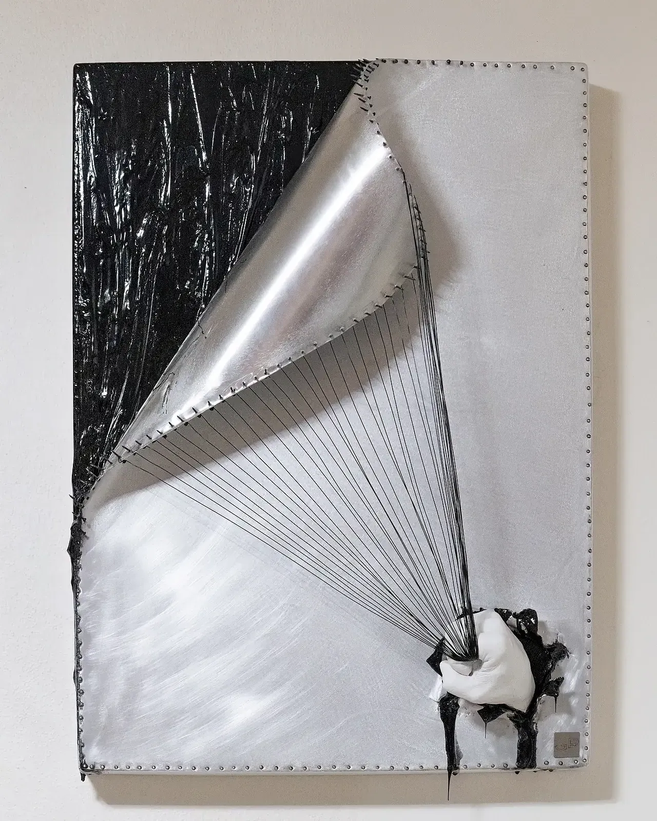 Scultura da parete con tecnica mista. L'opera è in resina epossidica, gesso ceramico e fili di alluminio nero. Nella parte inferiore a destra, c'è una mano che impugna i fili metallici collegati alla porzione dell'opera in alto a sinistra.