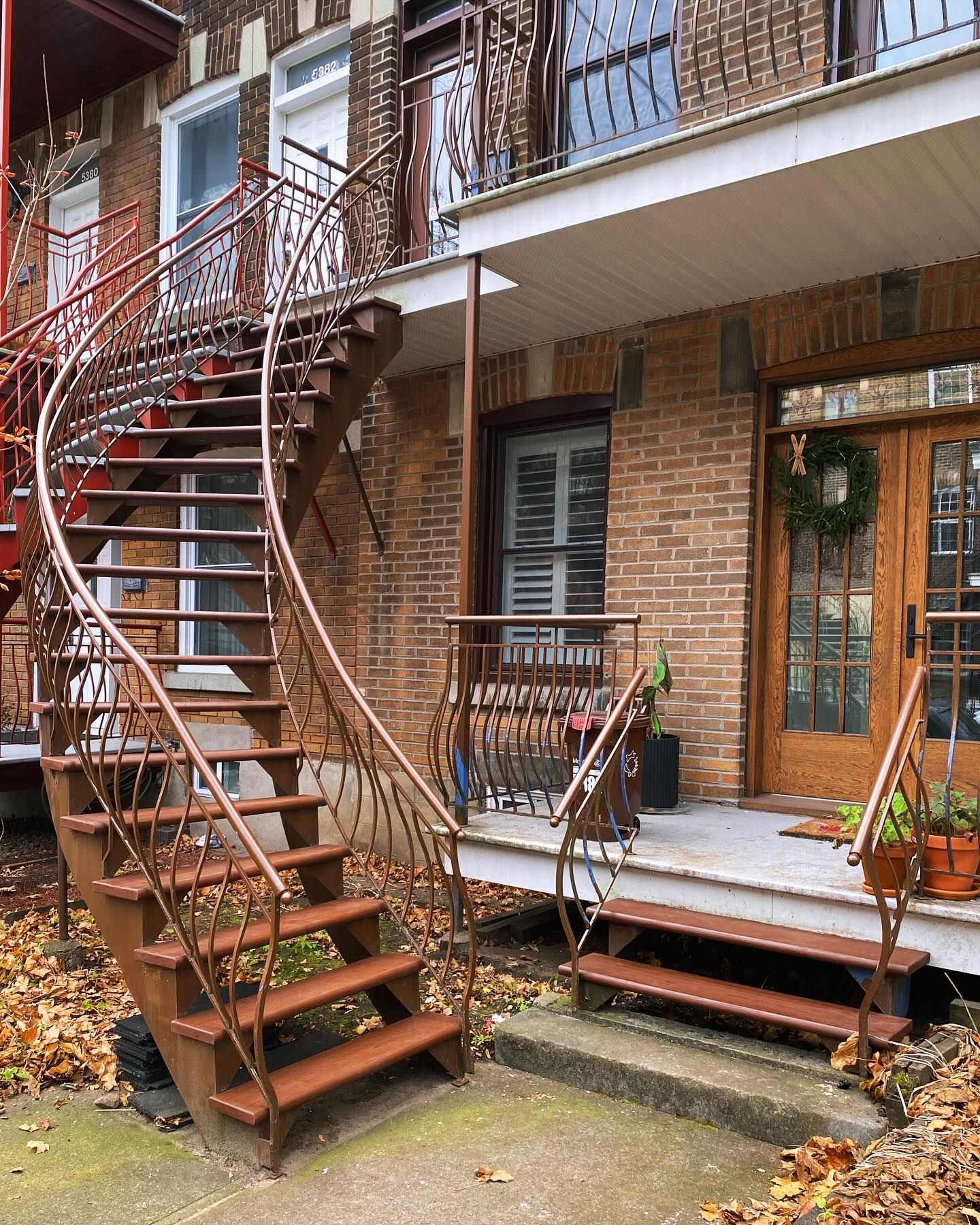 Brick apartment courtyard with metal spiral stairs, balconies, and a small porch with plants and chairs