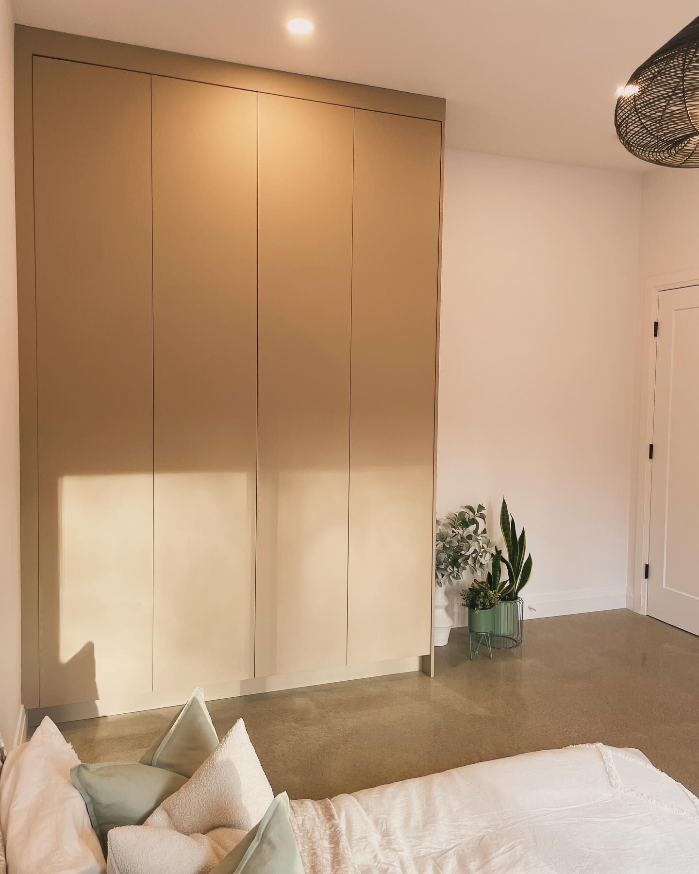 Minimal bedroom with tan built-in closet, white walls, plants, and a bed in the foreground