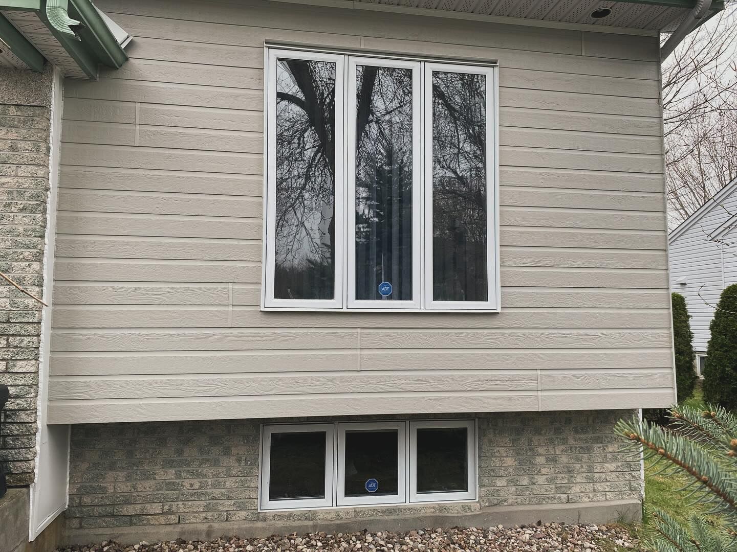 House exterior with beige siding and white-framed windows above a stone foundation