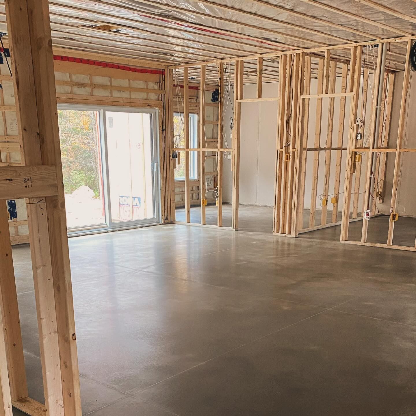 Unfinished room under construction with exposed wooden framing, concrete floor, and a sliding glass door.