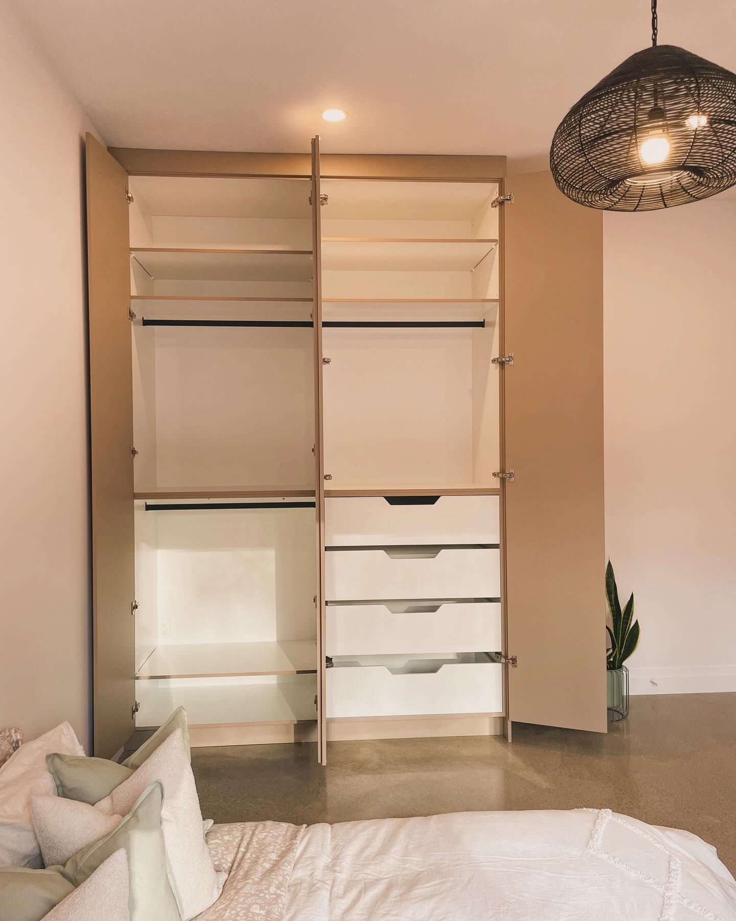 Minimalist bedroom closet with open shelving, drawers, and hanging rods beside a bed and pendant lamp.
