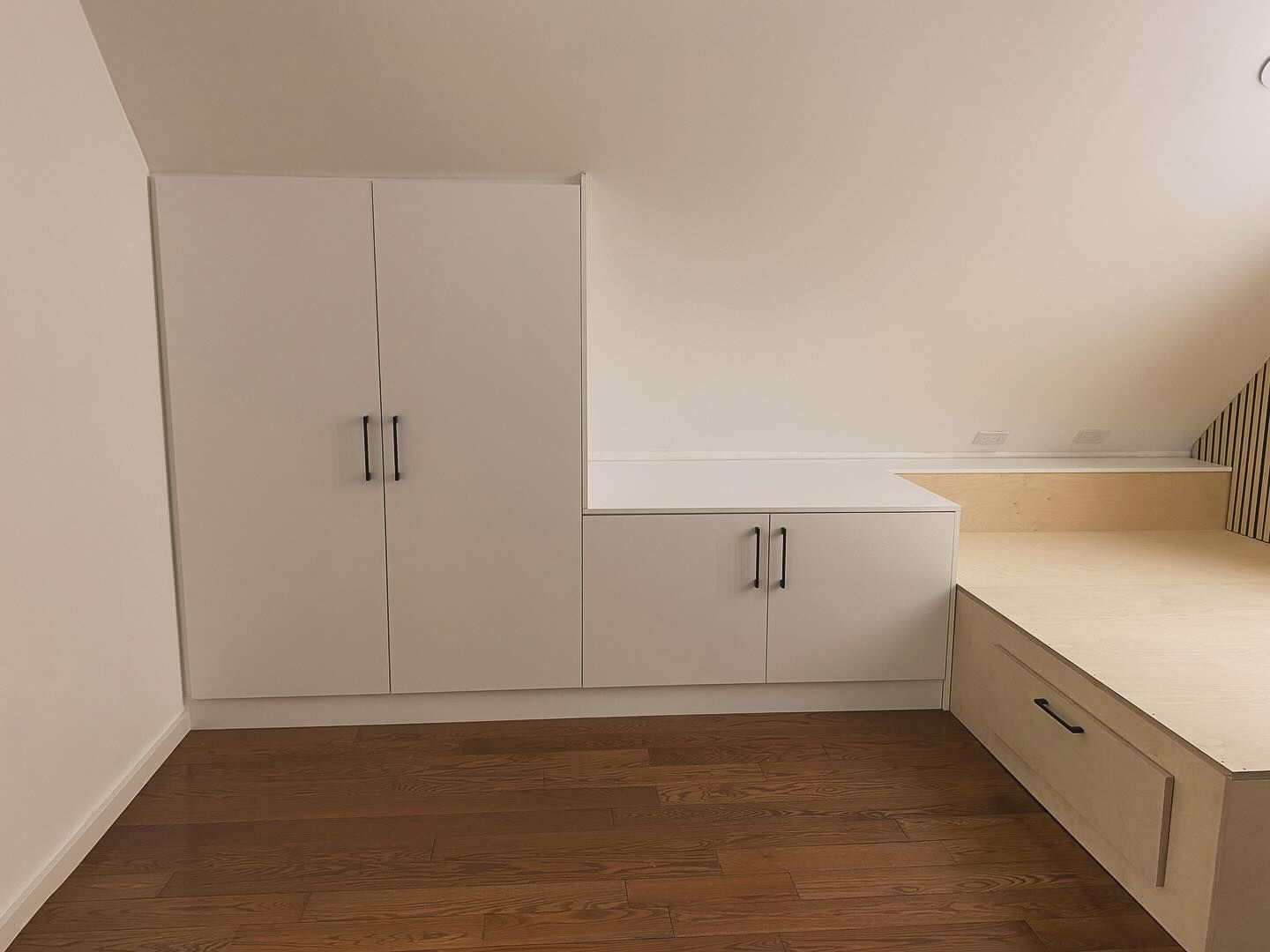White built-in cabinets and beige countertop in a small room with wood flooring.