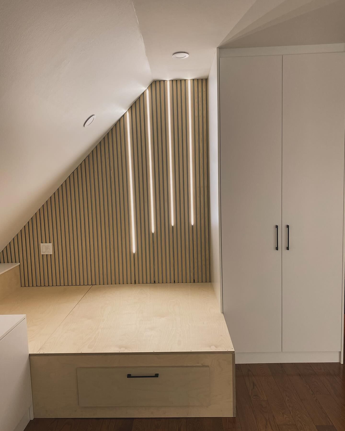 Loft bedroom with slanted ceiling, built-in wardrobe, and beige bed frame with vertical wood slats