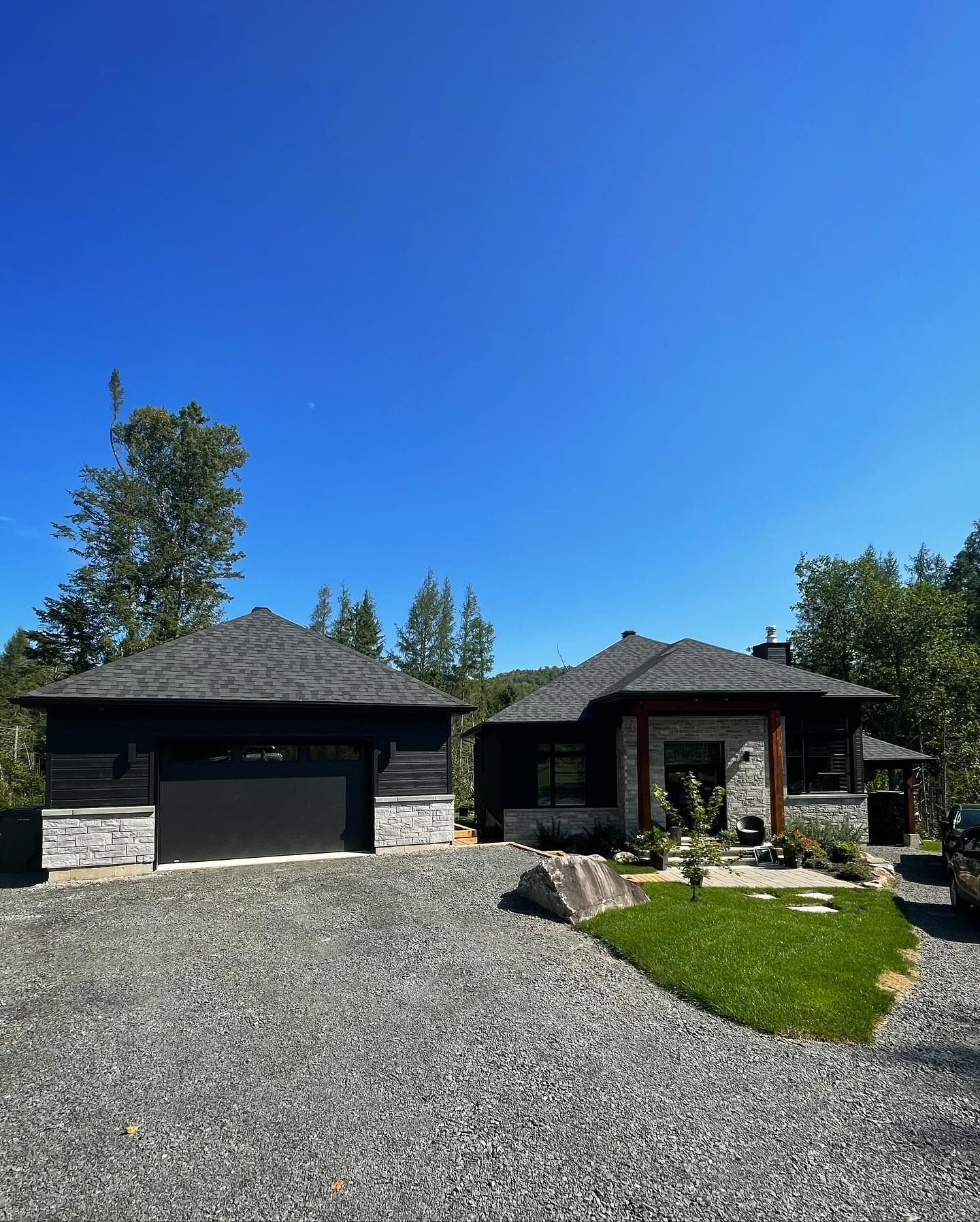 Single-story house with dark roof, garage, gravel driveway, and blue sky