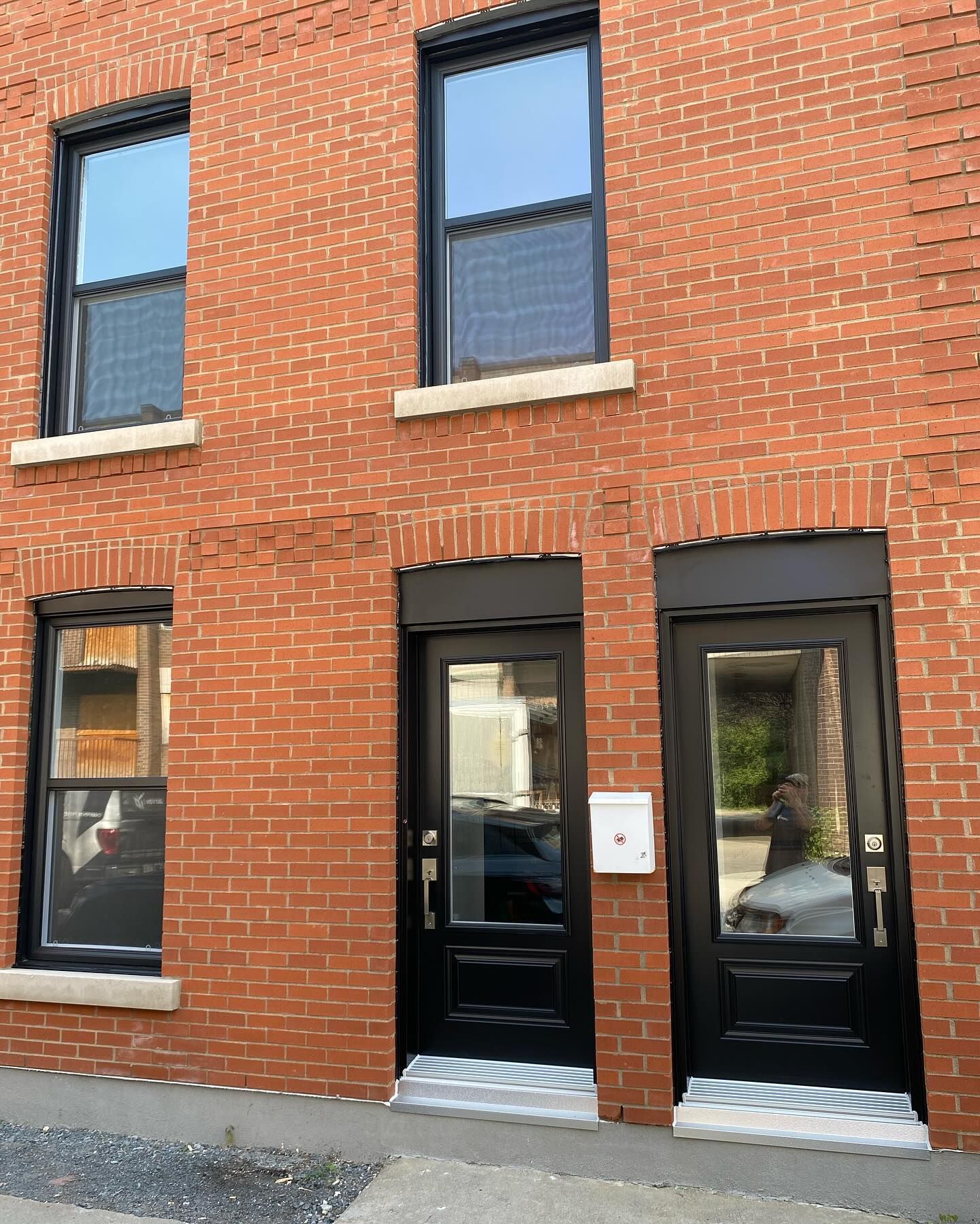 Red brick townhouse facade with black doors and windows, viewed from the street.