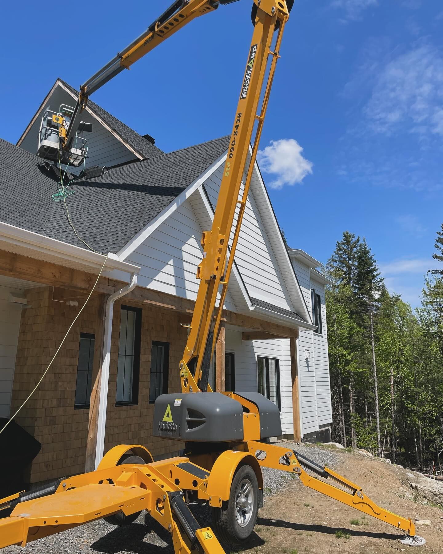 Yellow crane lifting roofing materials beside a house under construction on a sunny day