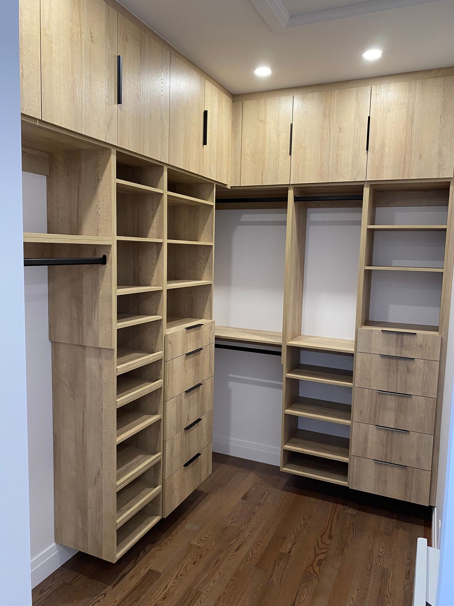 Walk-in closet with light wood shelving, drawers, hanging space, and dark wood floor