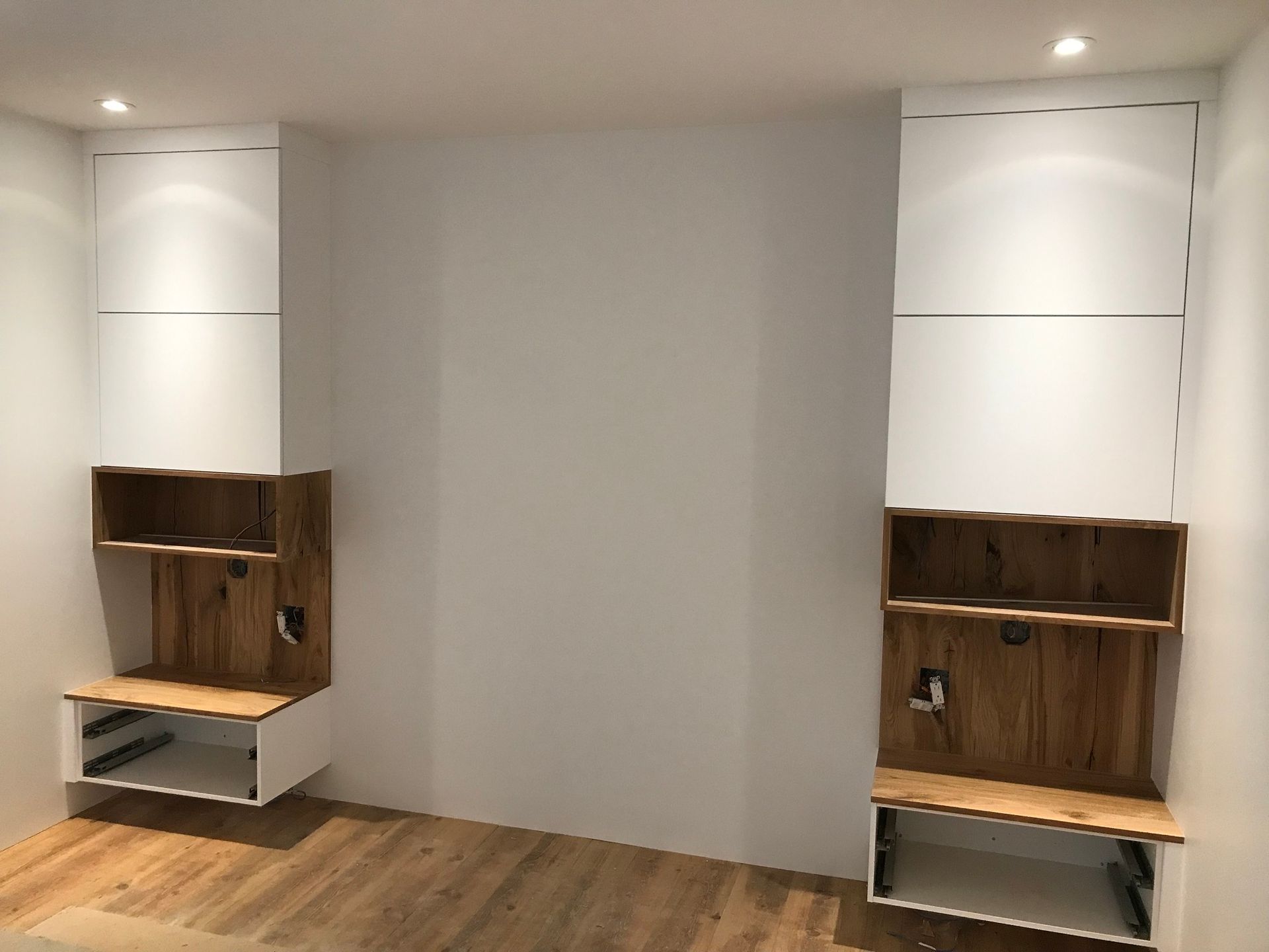 Built-in wood shelves and benches in a minimalist white room with recessed lights and wooden floor