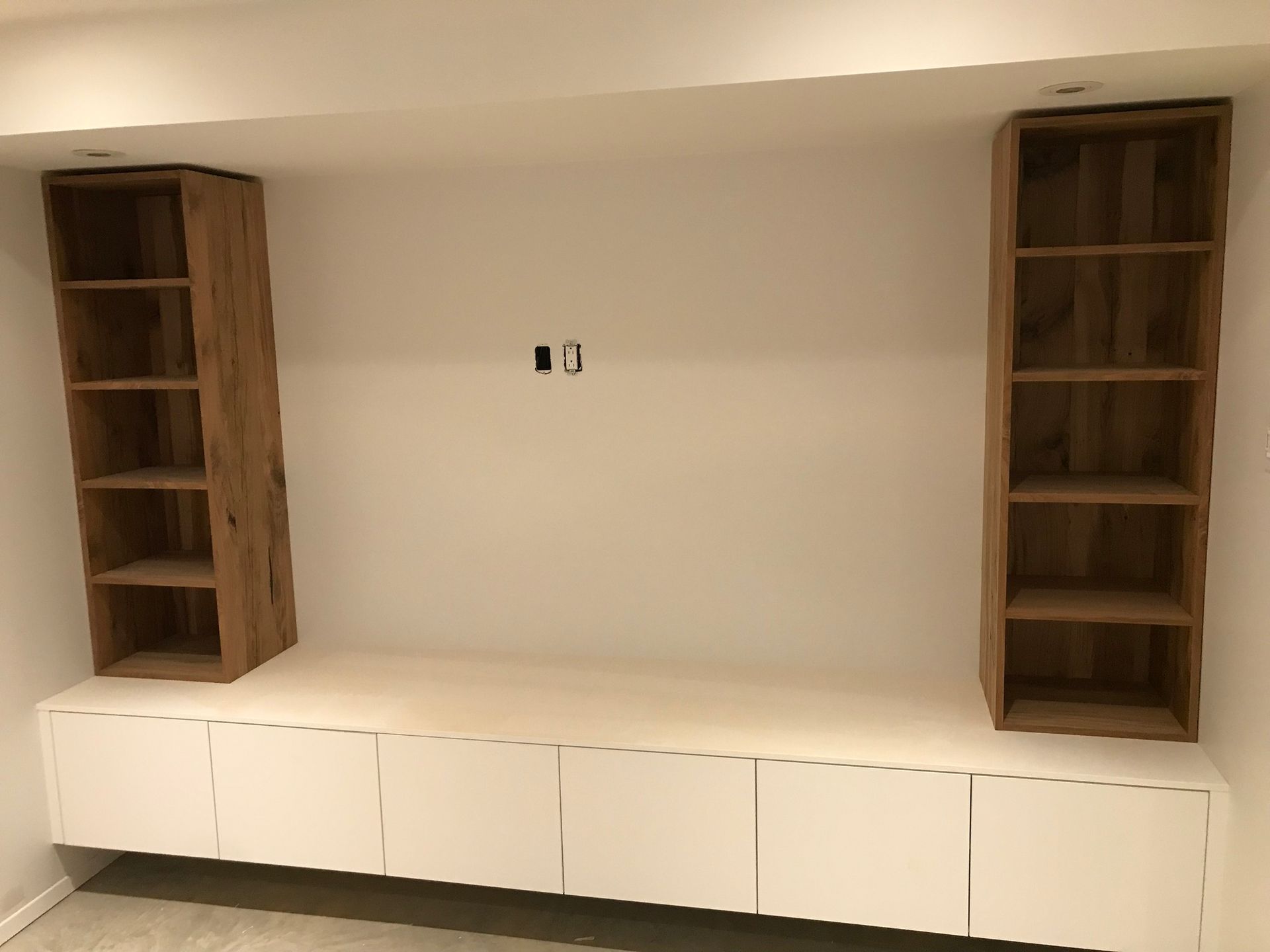 White built-in cabinet with two tall wooden shelves against a plain wall.