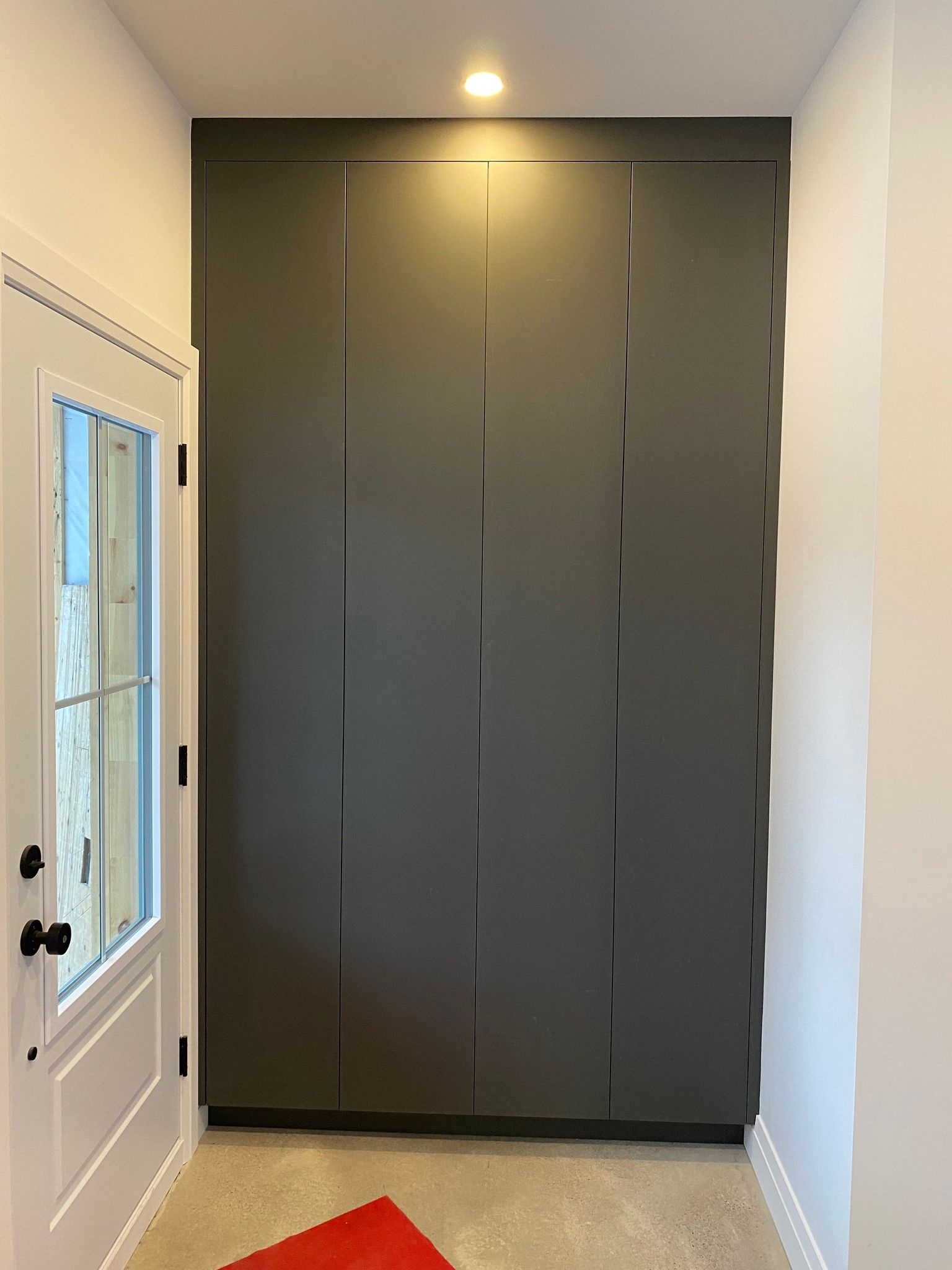 Narrow hallway with dark gray double closet doors, white walls, a window on the left, and recessed ceiling light.