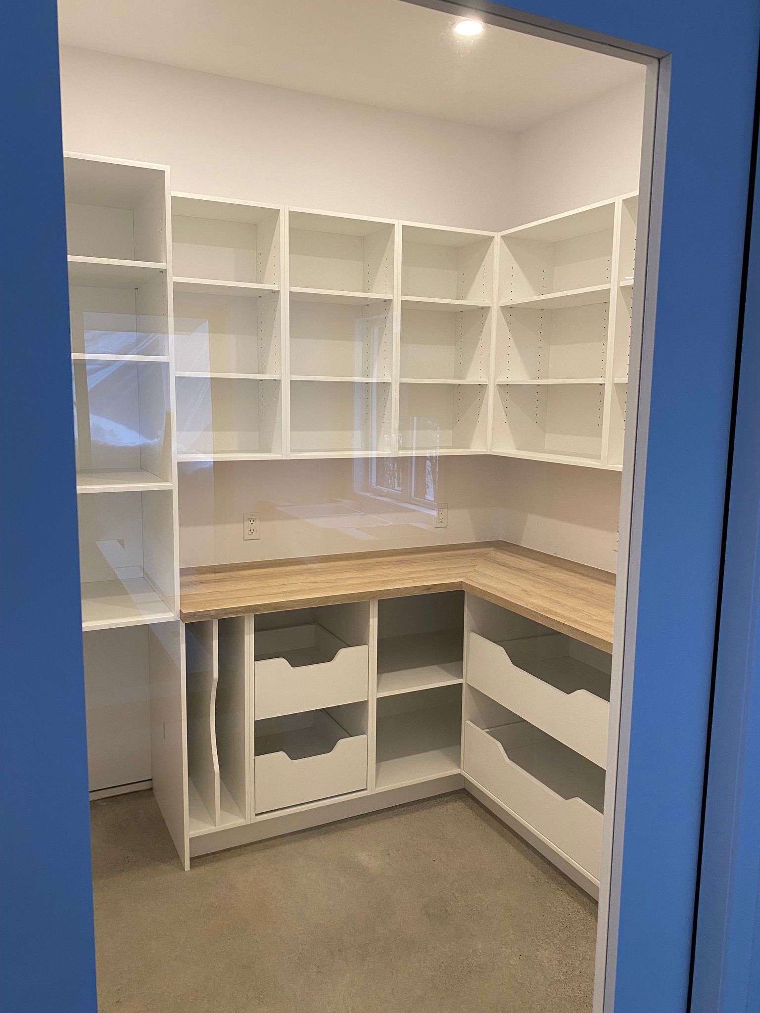 Empty white walk-in closet with built-in shelves, corner countertop, and open lower cabinets.