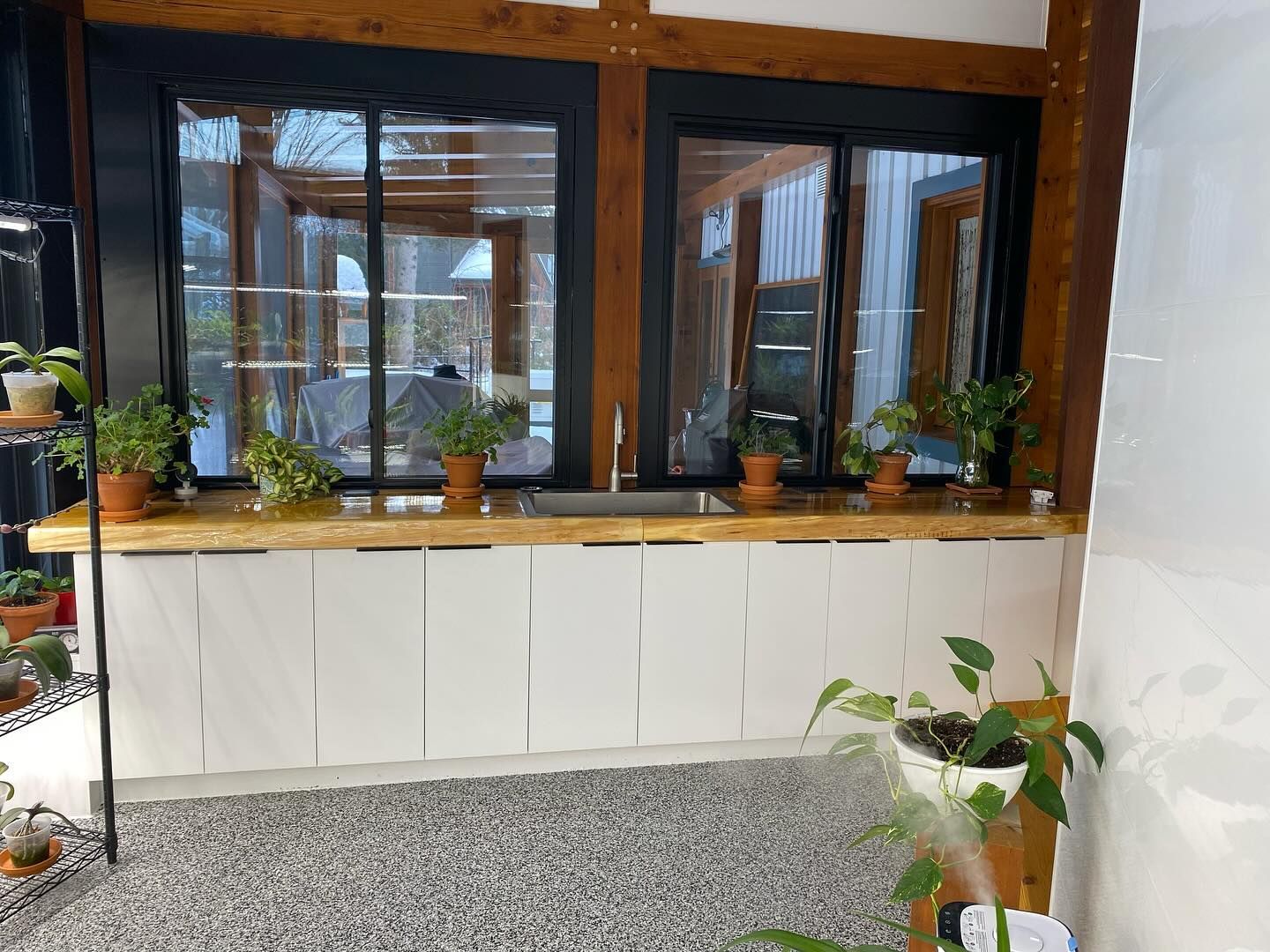 Plant-filled window nook with wooden frames, white cabinets, and a gray speckled floor