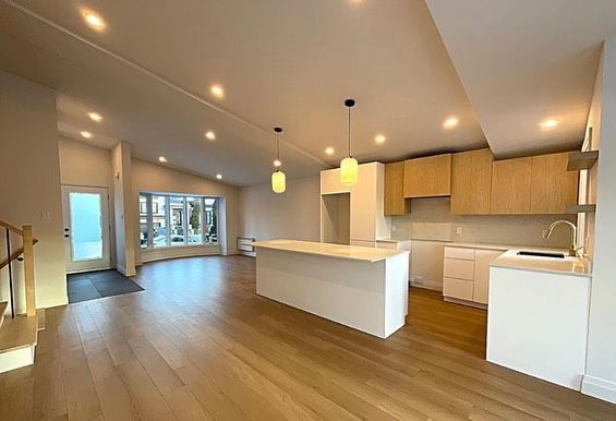 Modern open-plan kitchen and living room with wood floors, white island, and pendant lights