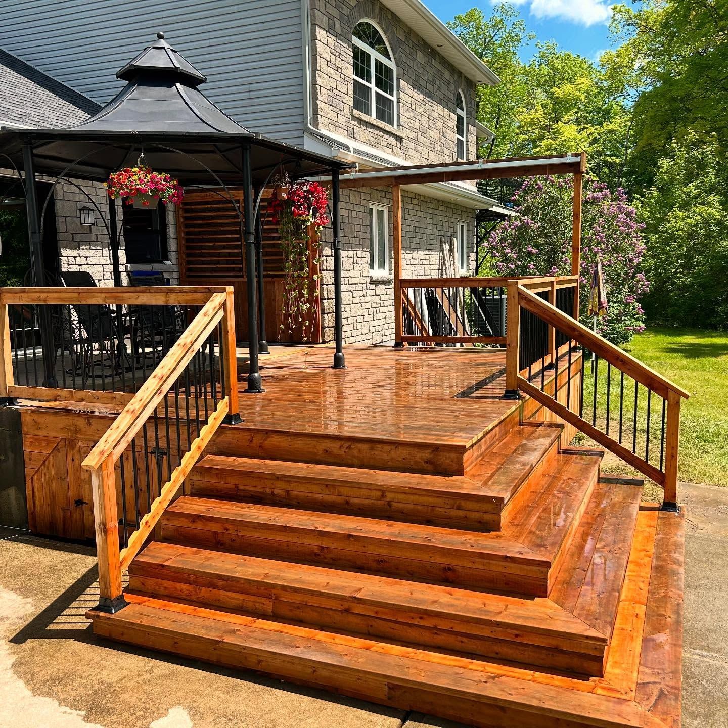 Wooden front porch and steps on a stone house, with black railings and hanging flower baskets.
