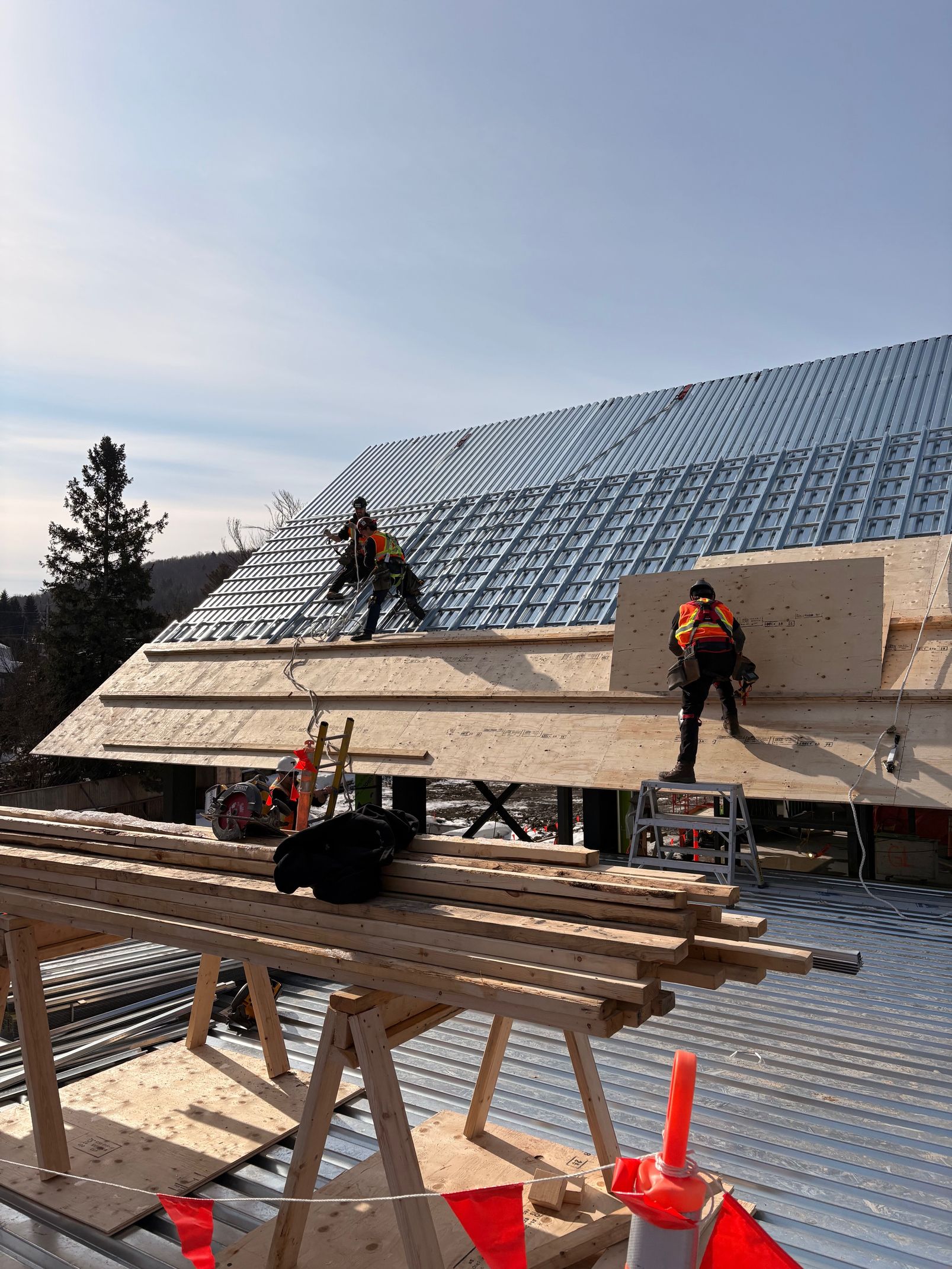 Workers installing solar panels on a steep roof, with stacks of panels and safety cones in the foreground.