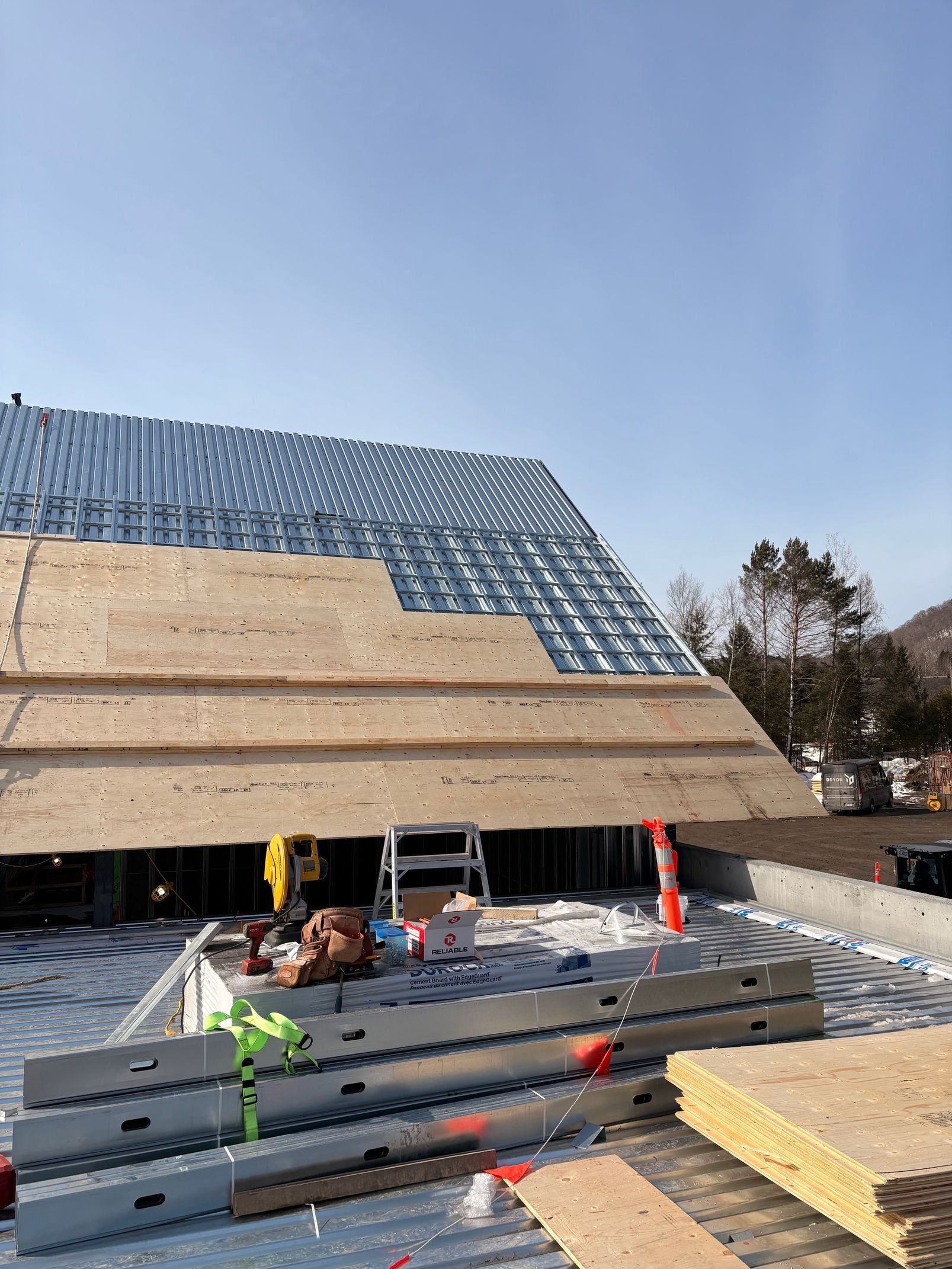 Construction site with a large roof under assembly, stacked panels, and workers on a sunny day