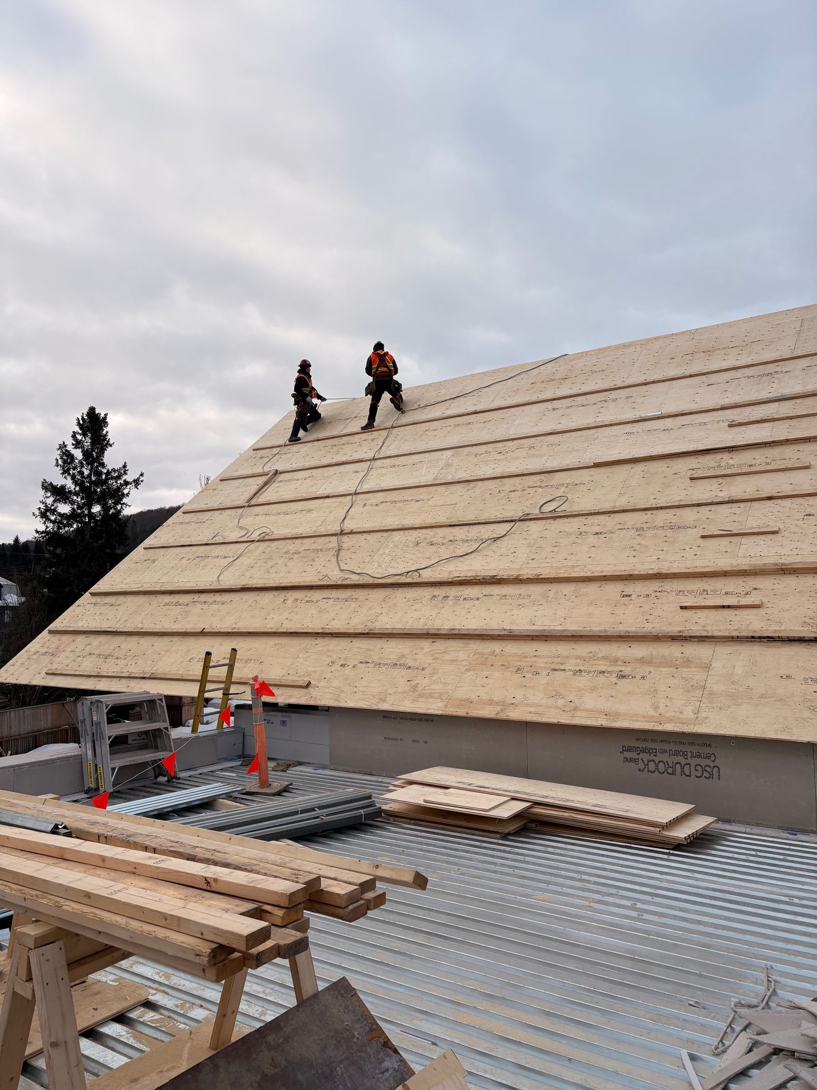 Workers on a sloped roof under construction, with materials and tools in the foreground.