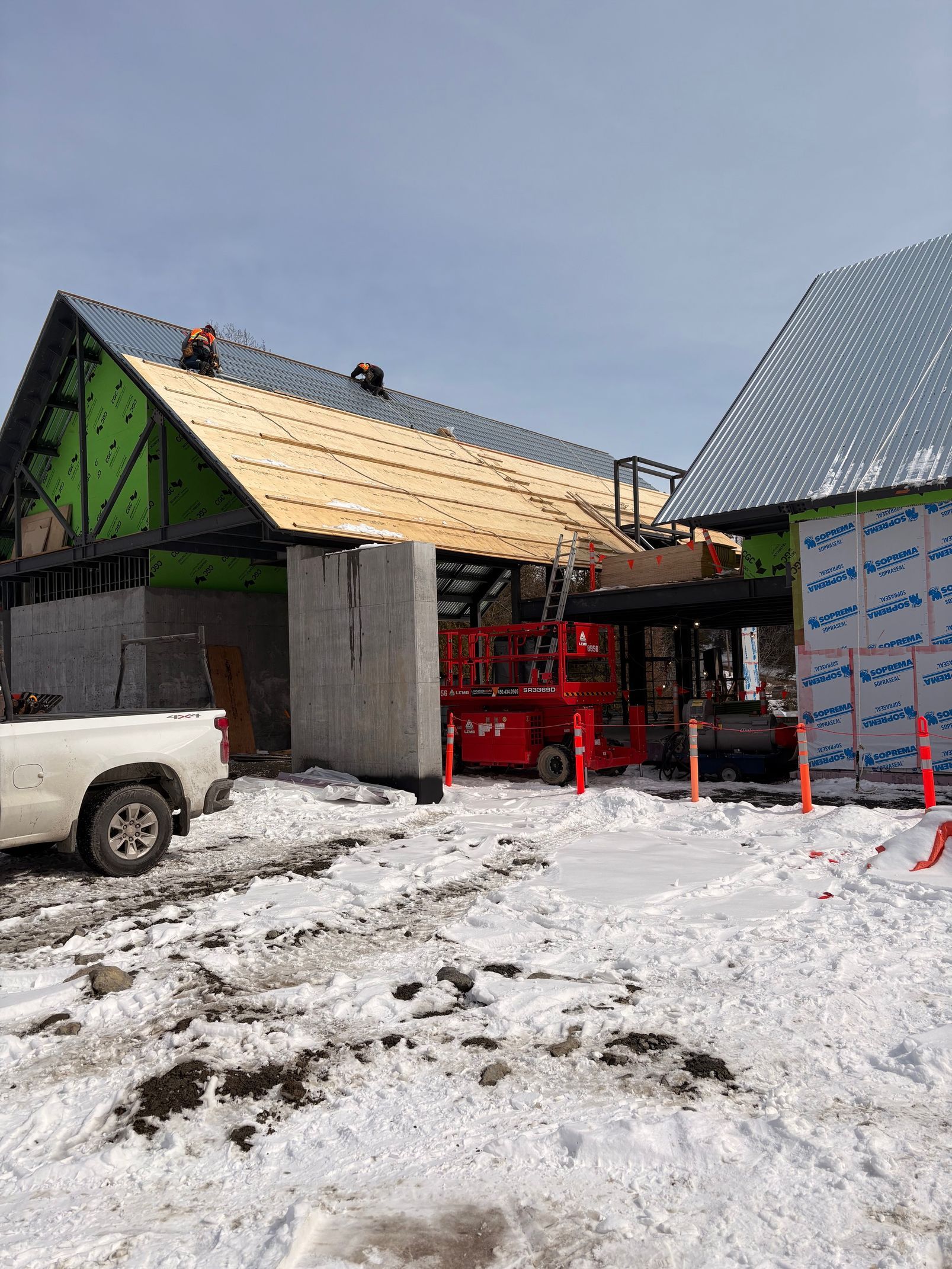 Snowy construction site with roof framing, red lift, and a white pickup truck