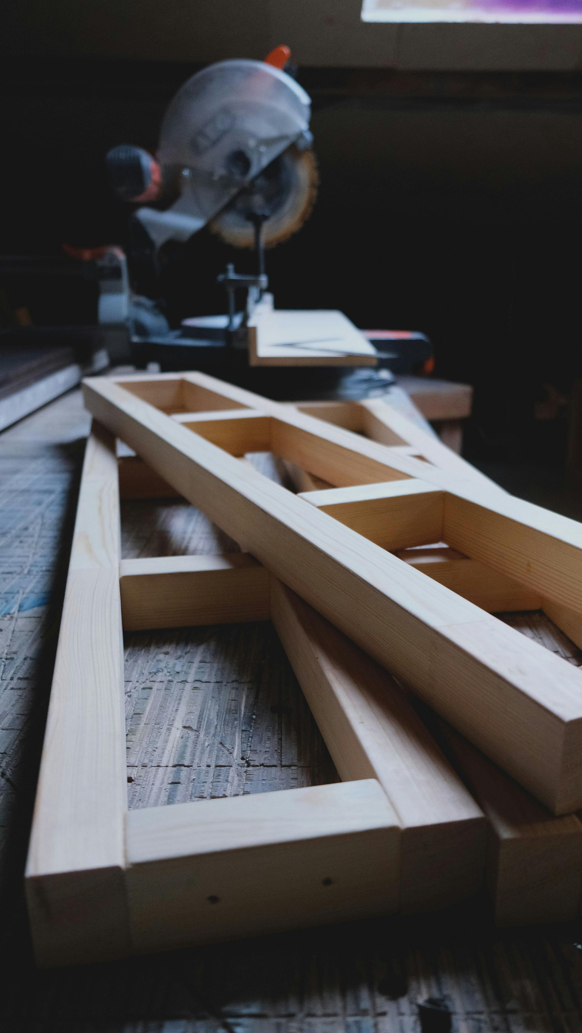 Wooden frame pieces on a table with a miter saw in the background