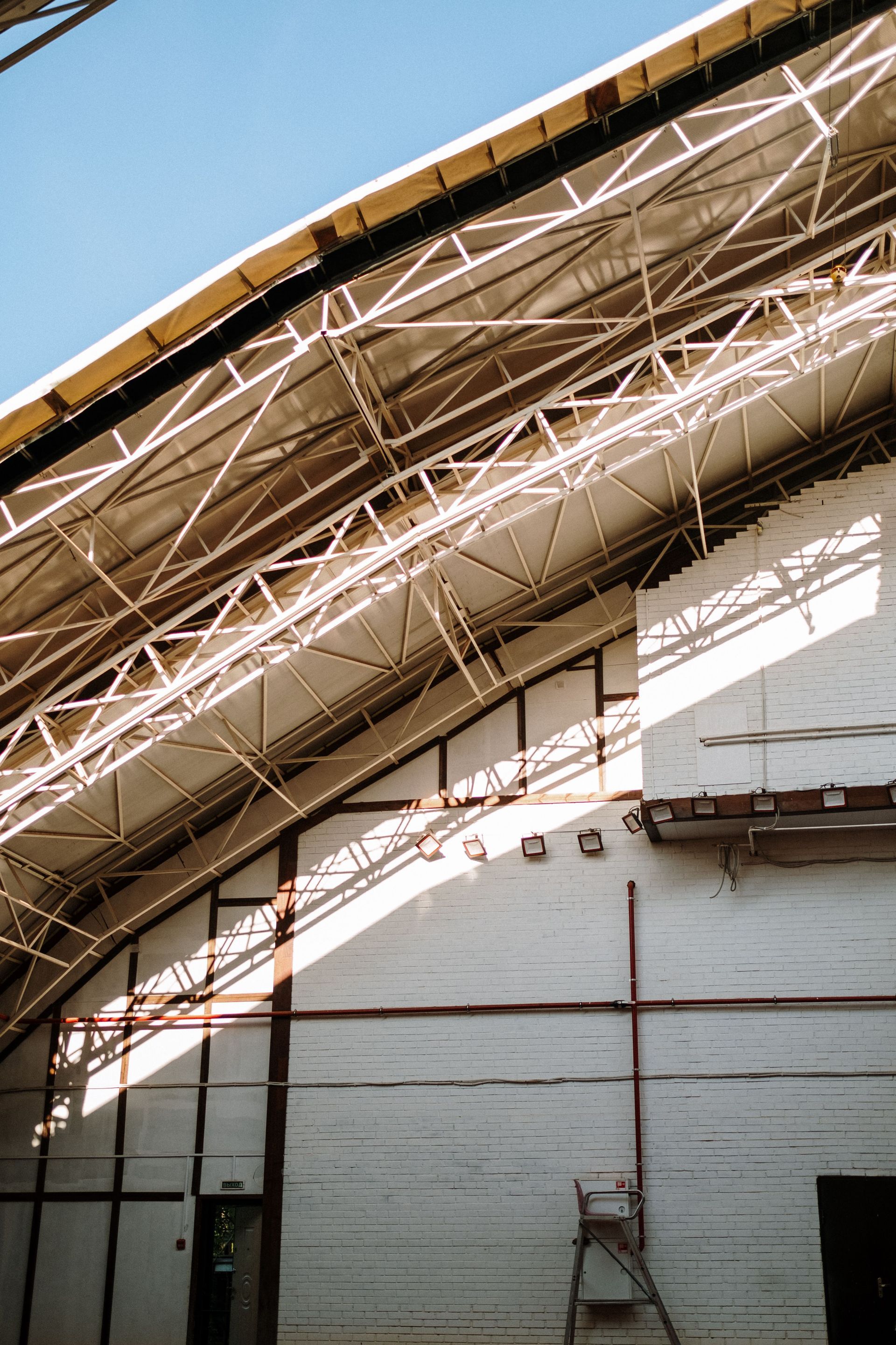Curved roof trusses over a white wall and ladder inside an industrial building