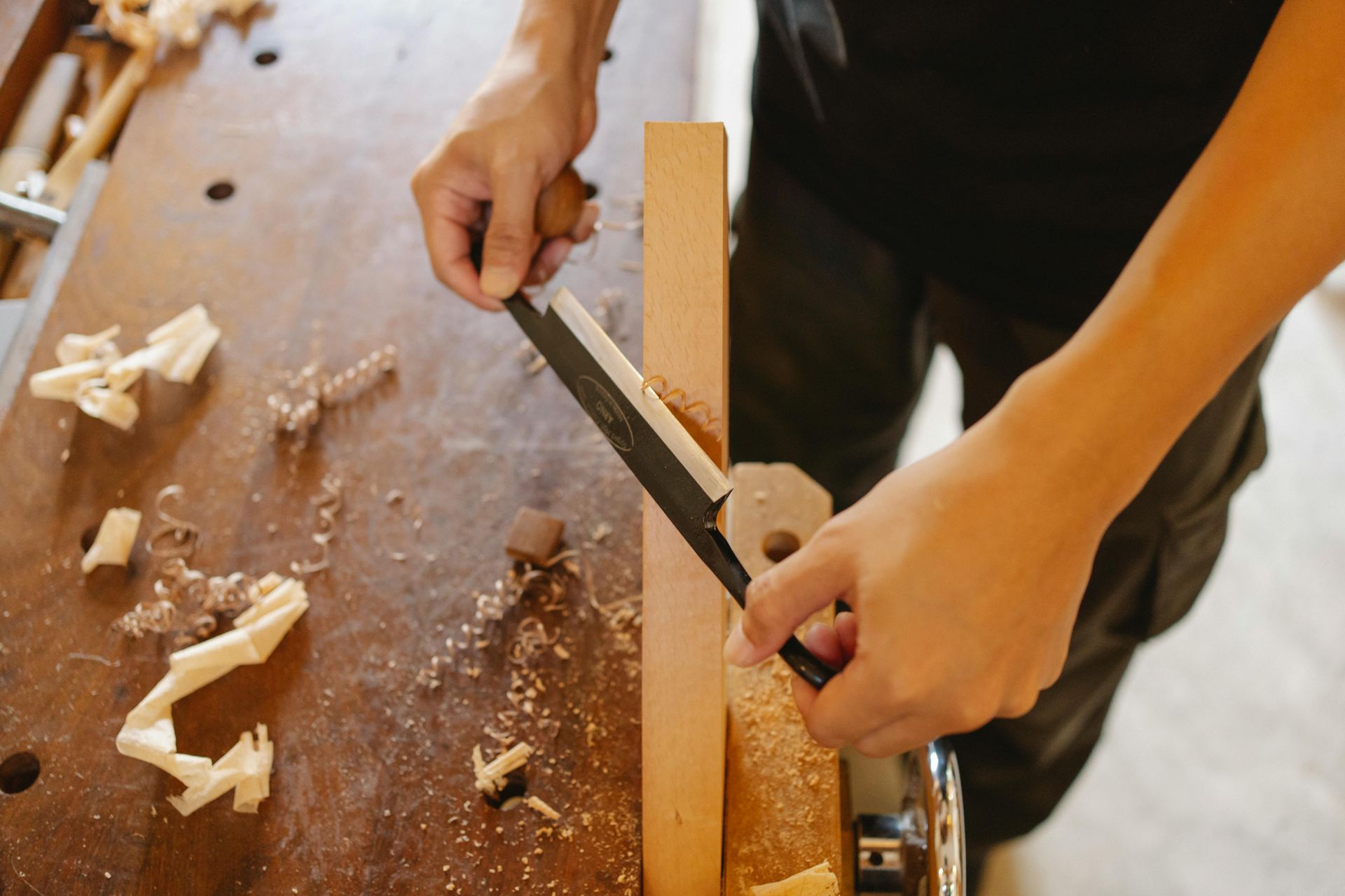 Hands using a hand plane to smooth a wooden board on a cluttered workbench