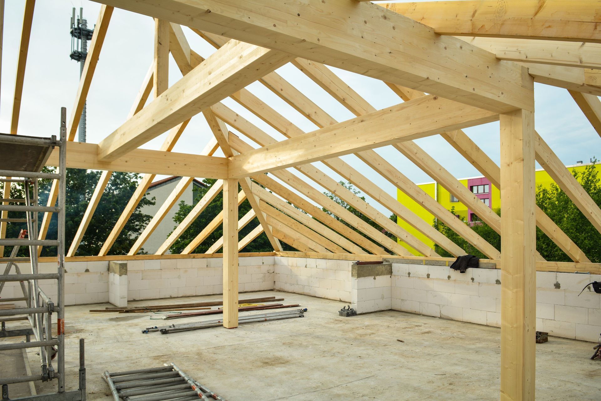 Timber roof frame under construction on a concrete building shell, with scaffolding and skylight openings