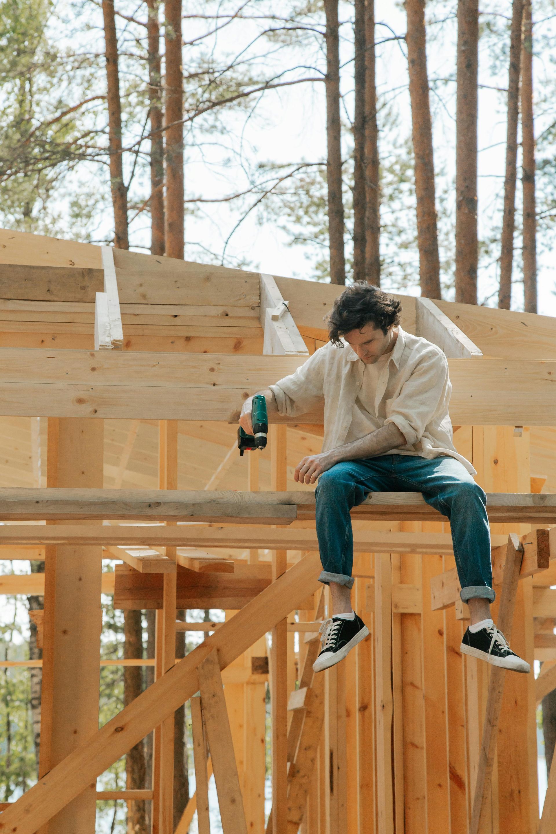 Construction worker sitting on a wooden frame, holding a power tool at a house build site.