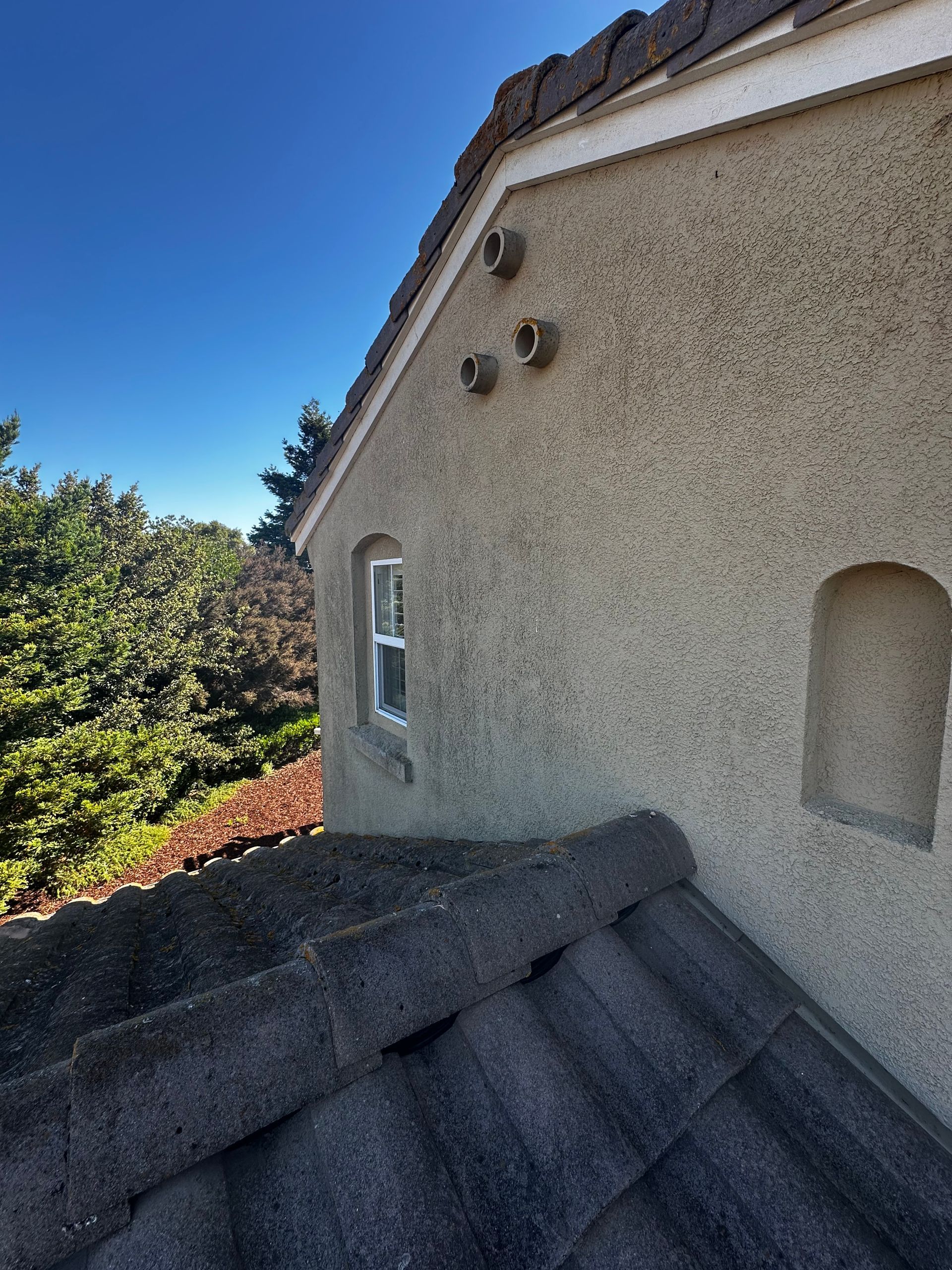 Exterior of a stucco building with three vents, small window, arched alcove, and tiled roof.