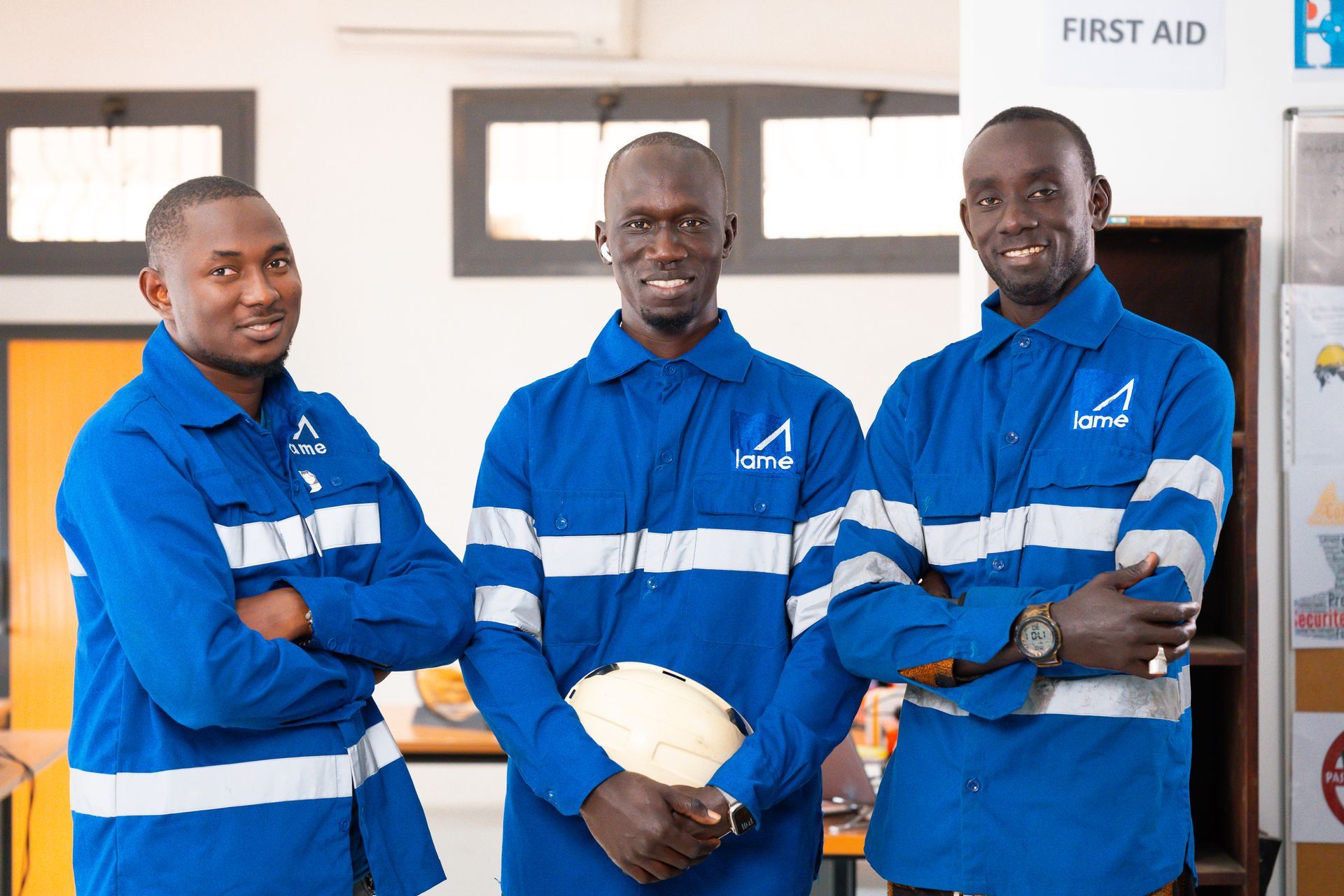 Three men in blue work uniforms, arms crossed, smiling. 
