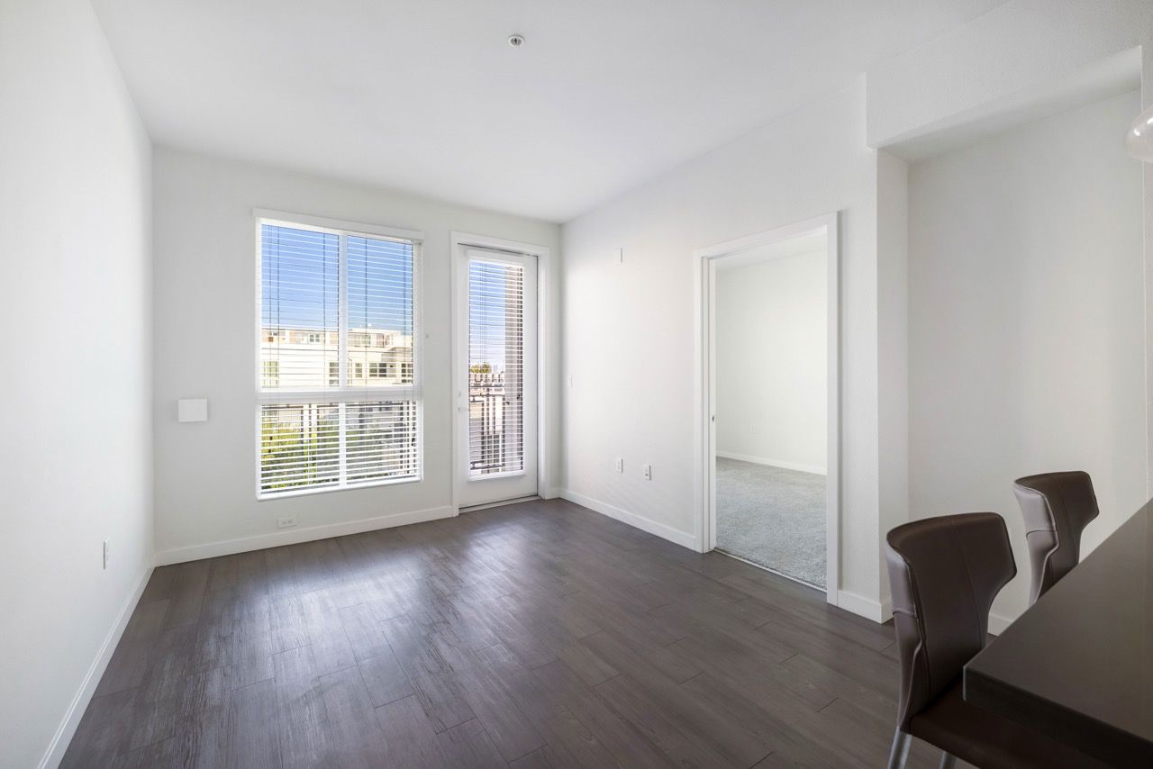 Bright living area with large windows, white walls, and a doorway to another room.